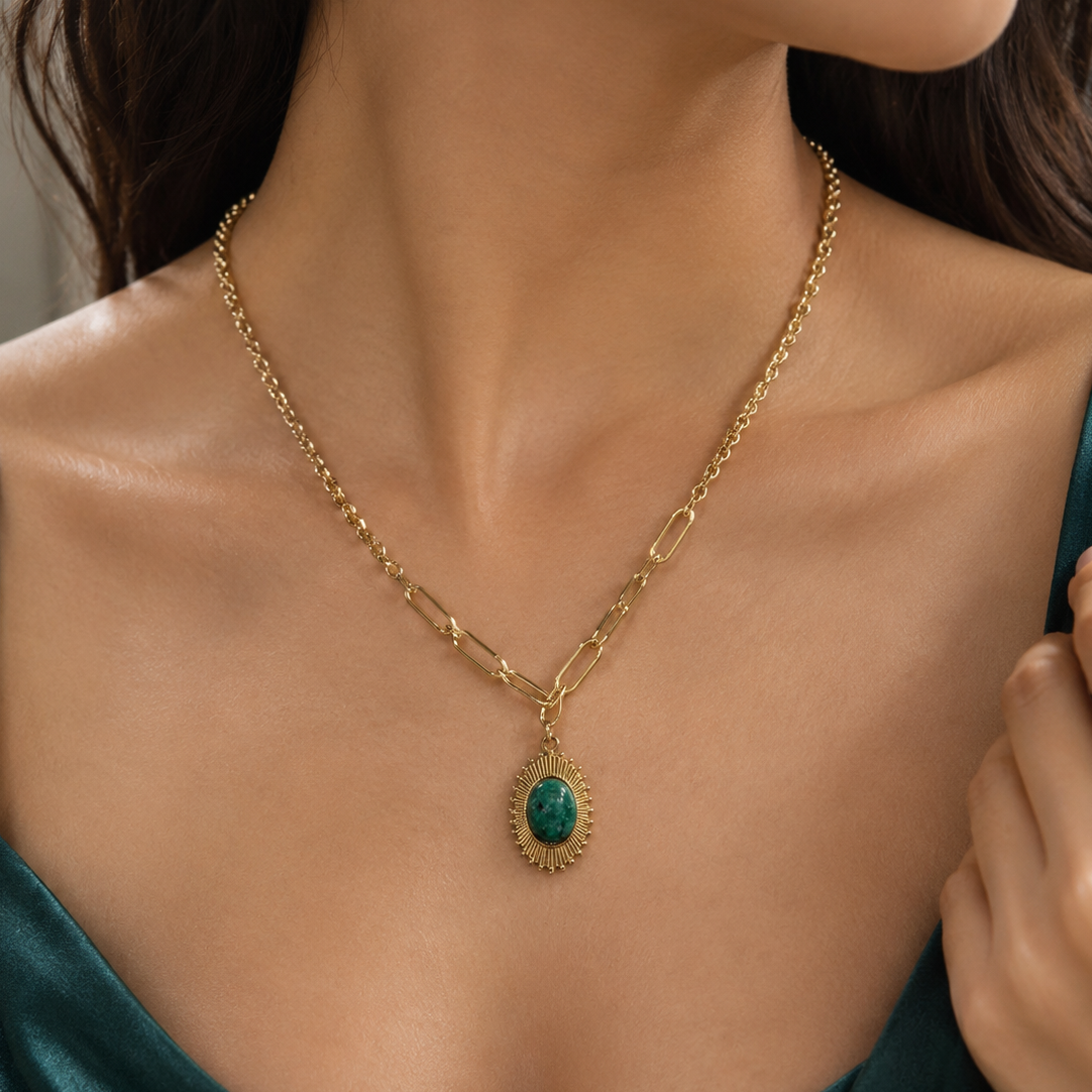 Oval green stone necklace with textured pendant frame and dual chain design by Civaro
A close-up of a model wearing a gold chain necklace with a teardrop-shaped green stone pendant.