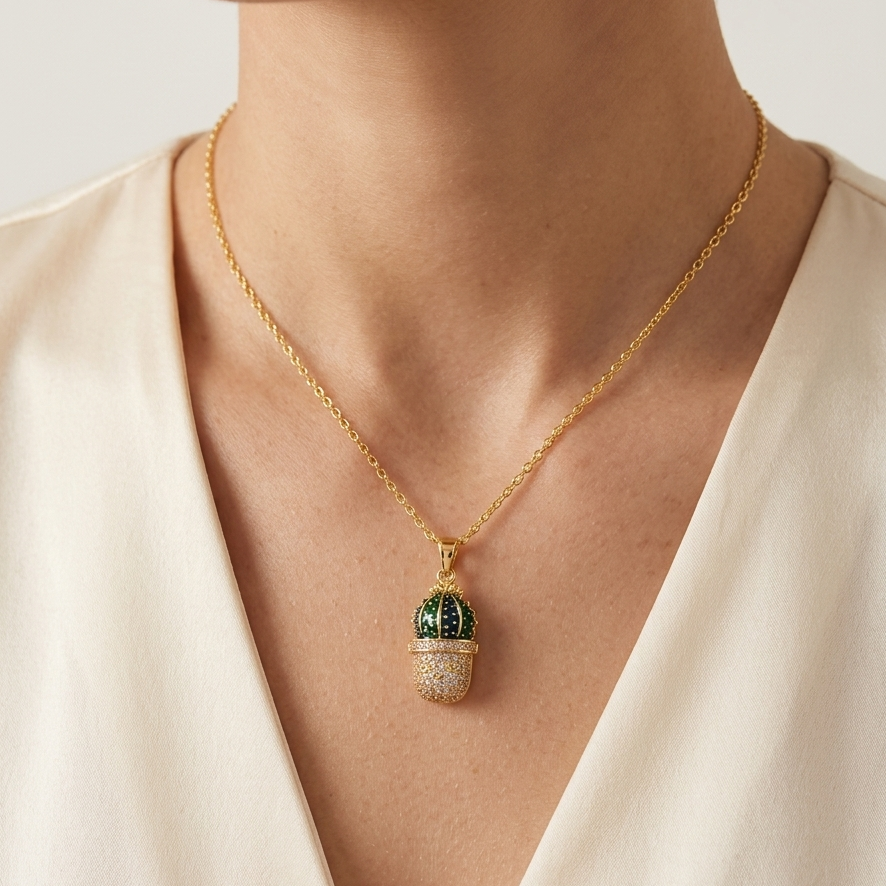 A gold chain necklace with a cactus-shaped pendant, worn by a model in a cream-colored top. The pendant features a green top section and a textured, light-colored bottom section by Civaro