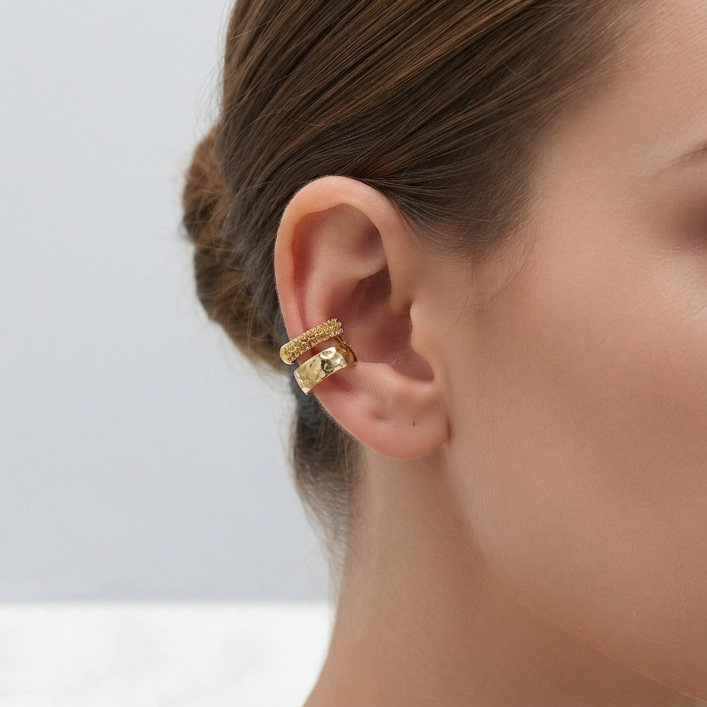 A close-up of a model's ear wearing a pair of stacked gold ear cuffs with textured and smooth surfaces by Civaro