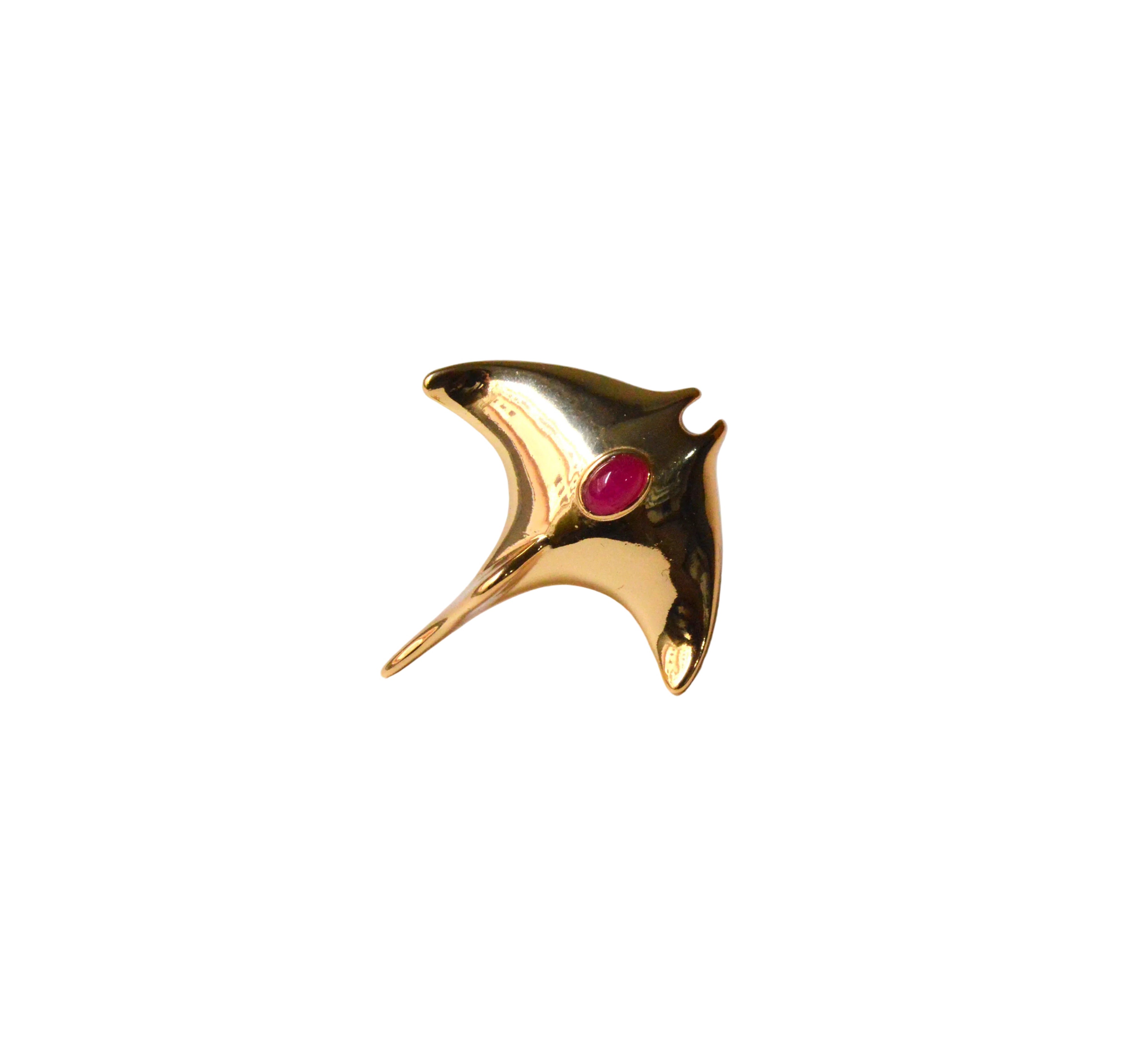 Gold fish-shaped brooch with a red gemstone on a light gray background