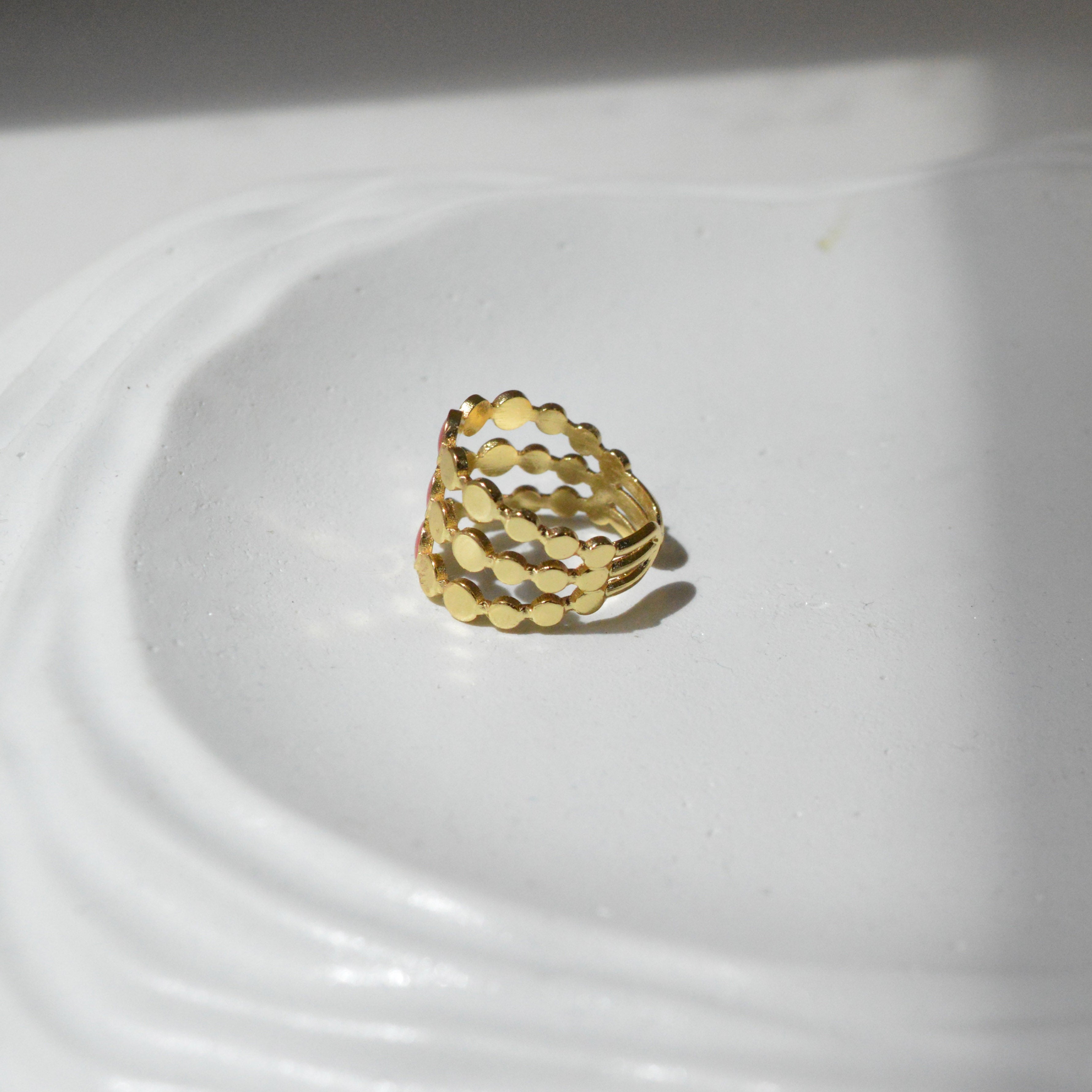 Close up of the smooth red enamel cells and slightly adjustable open band of the Crimson Signet cage ring held in hand