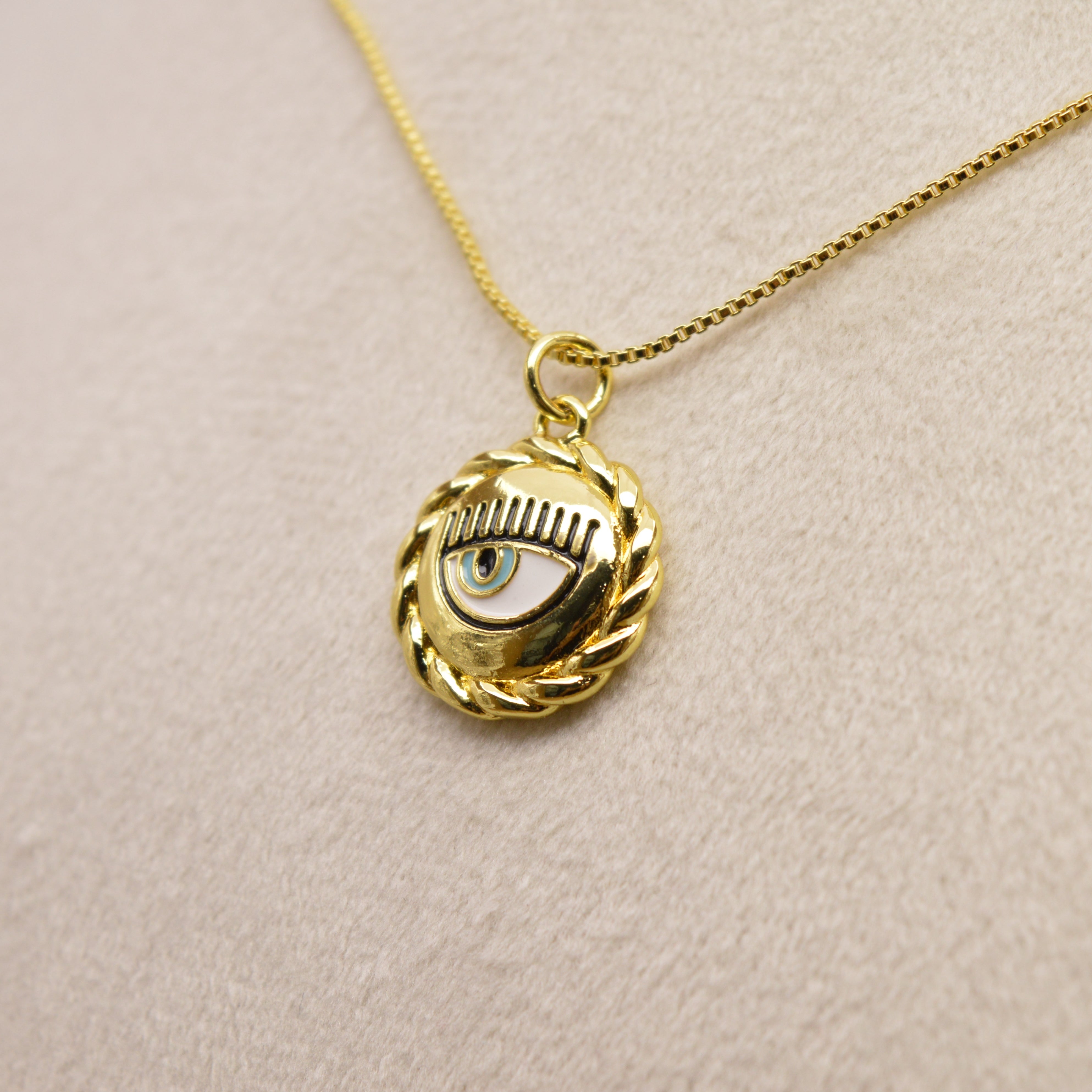 Close-up of gold evil eye pendant featuring circular rope-inspired detailing