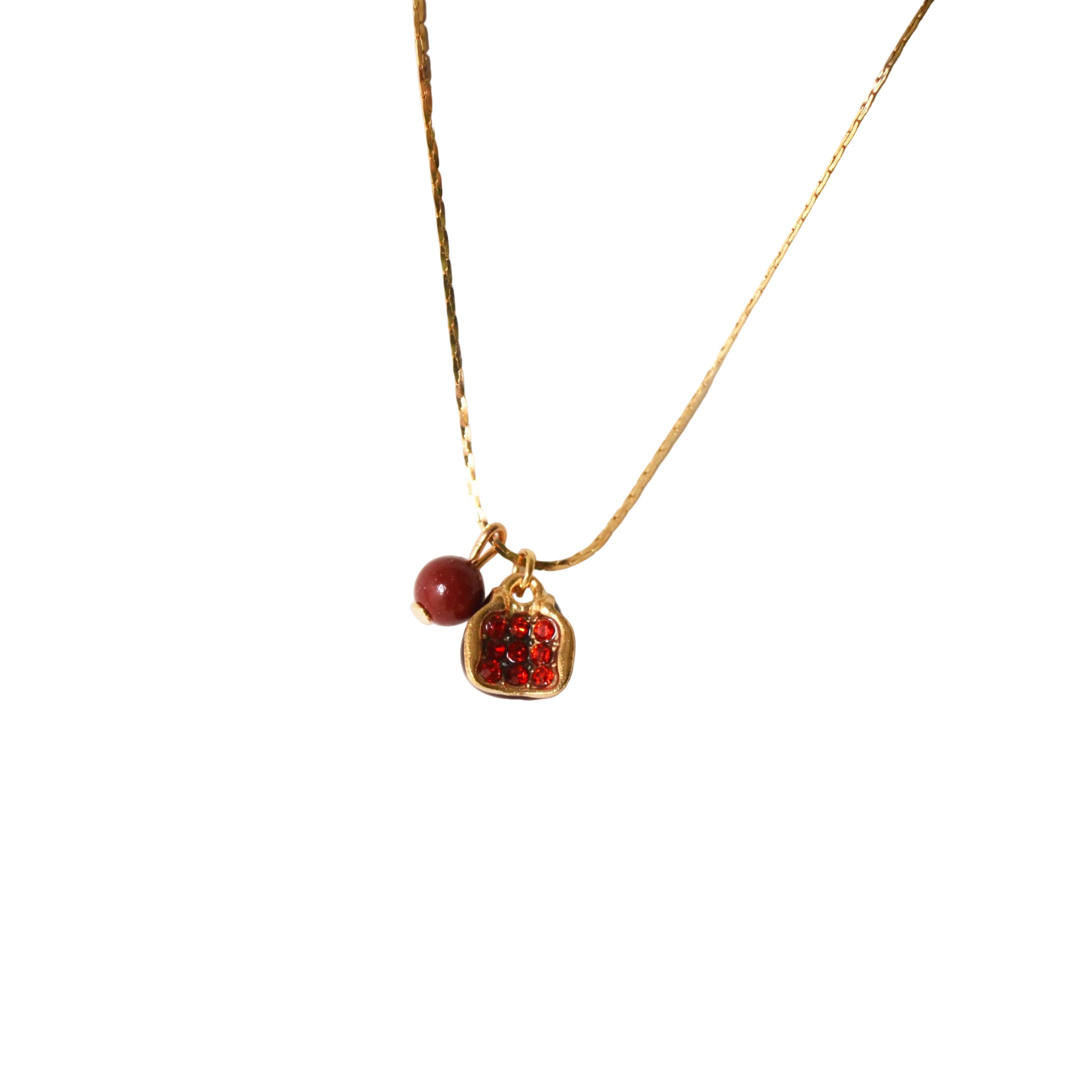 A gold chain necklace featuring a small red bead charm and a textured red heart-shaped pendant, displayed against a solid white background.