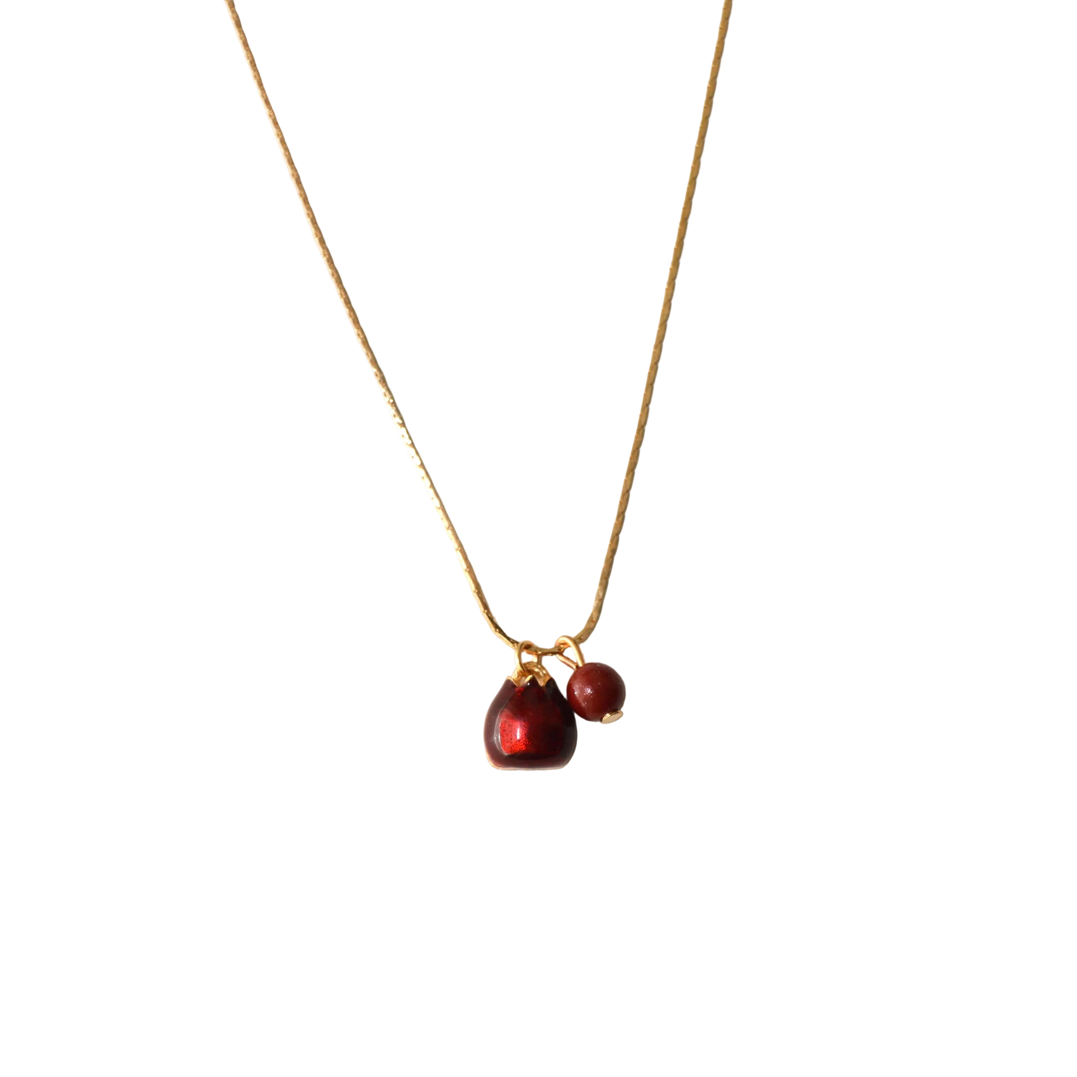 A delicate gold chain necklace featuring a teardrop-shaped dark red gemstone pendant and a small round red bead charm, displayed against a plain off-white background.