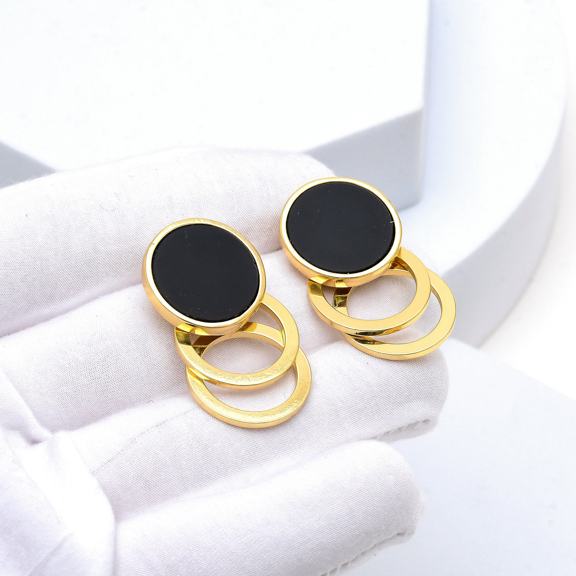 Close up of the polished 18k gold plating and smooth enamel on the Onyx Cascade earrings held in hand
