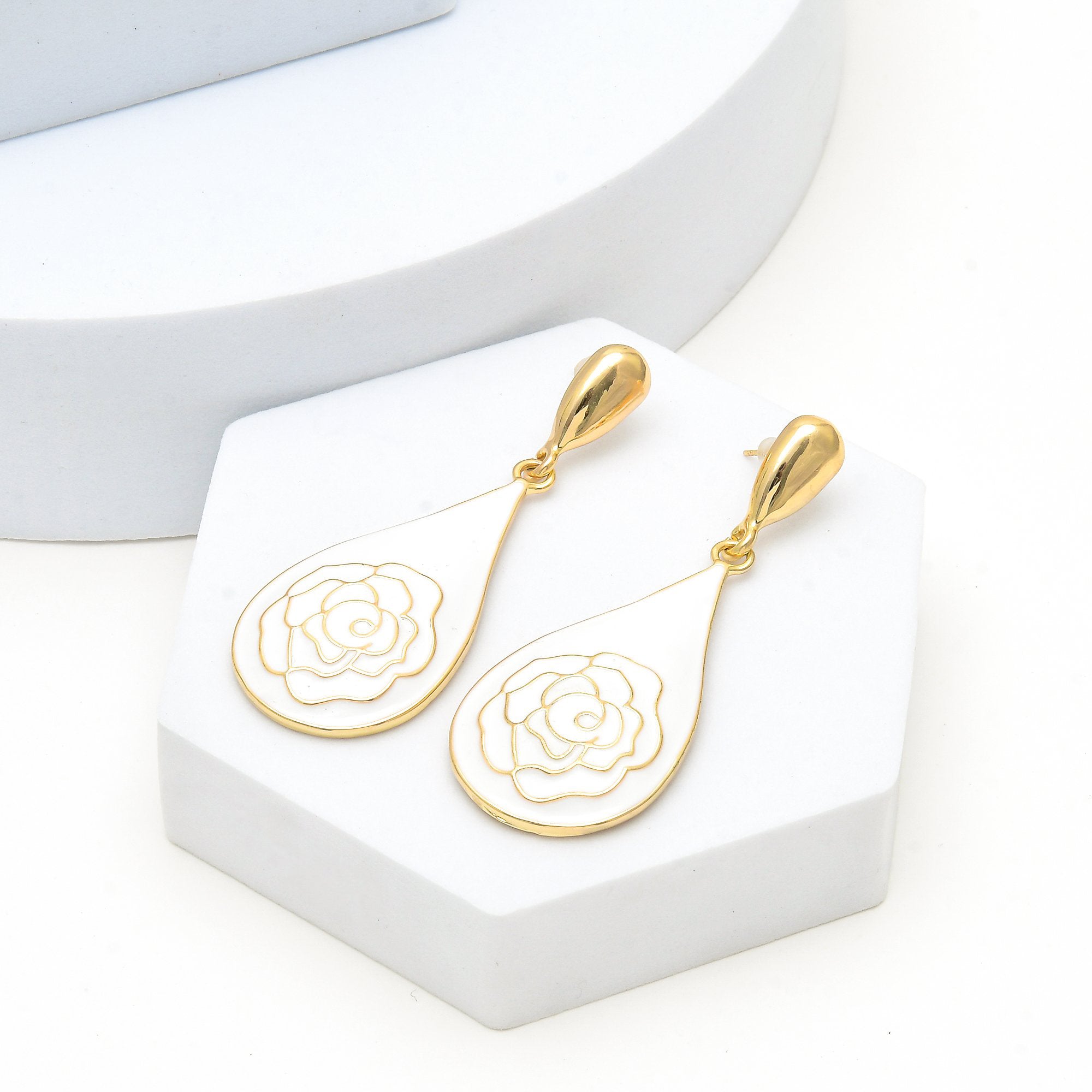 Pair of gold and white enamel rose earrings displayed on a minimalist architectural tier