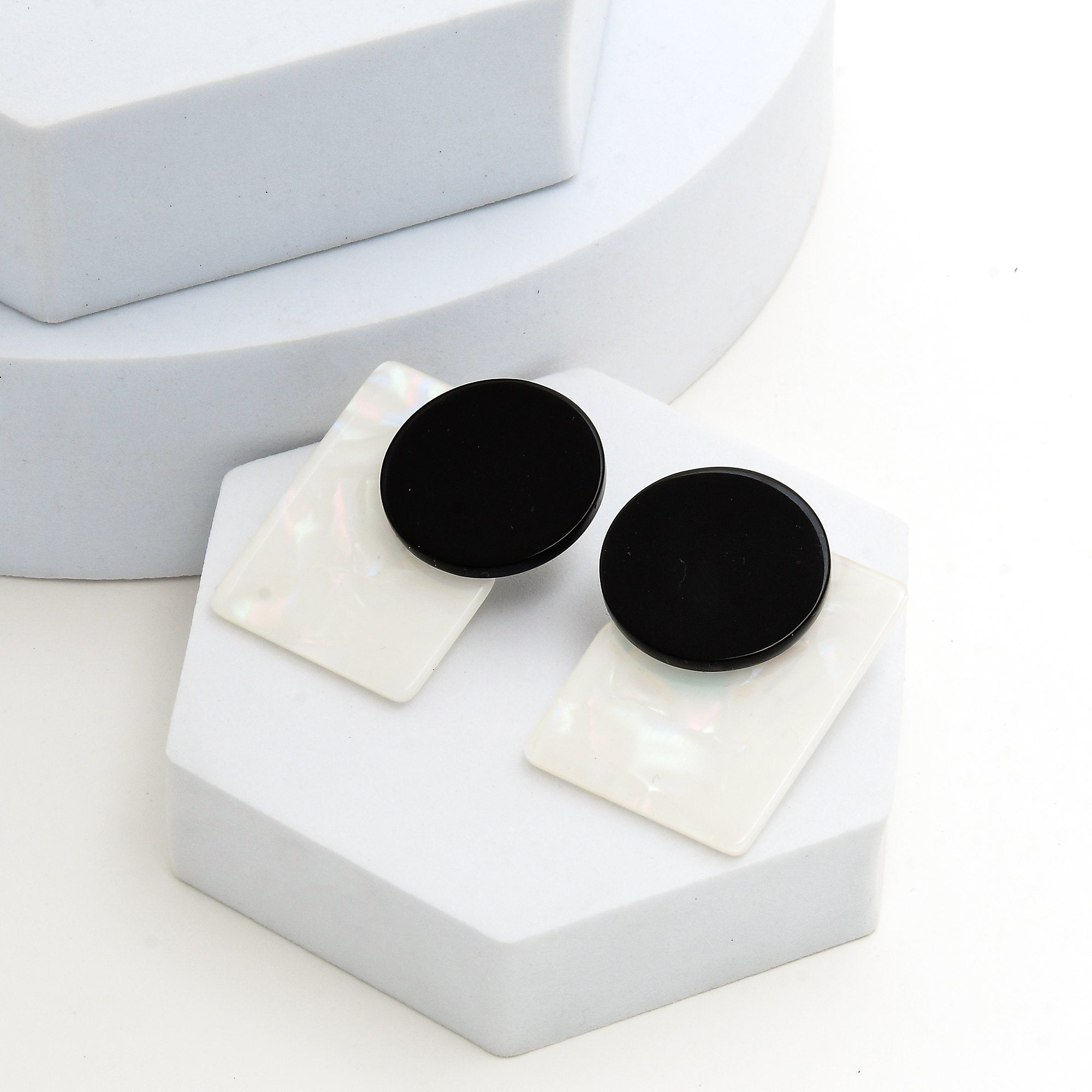 Pair of black and white abstract geometric resin earrings displayed on a minimalist architectural tier