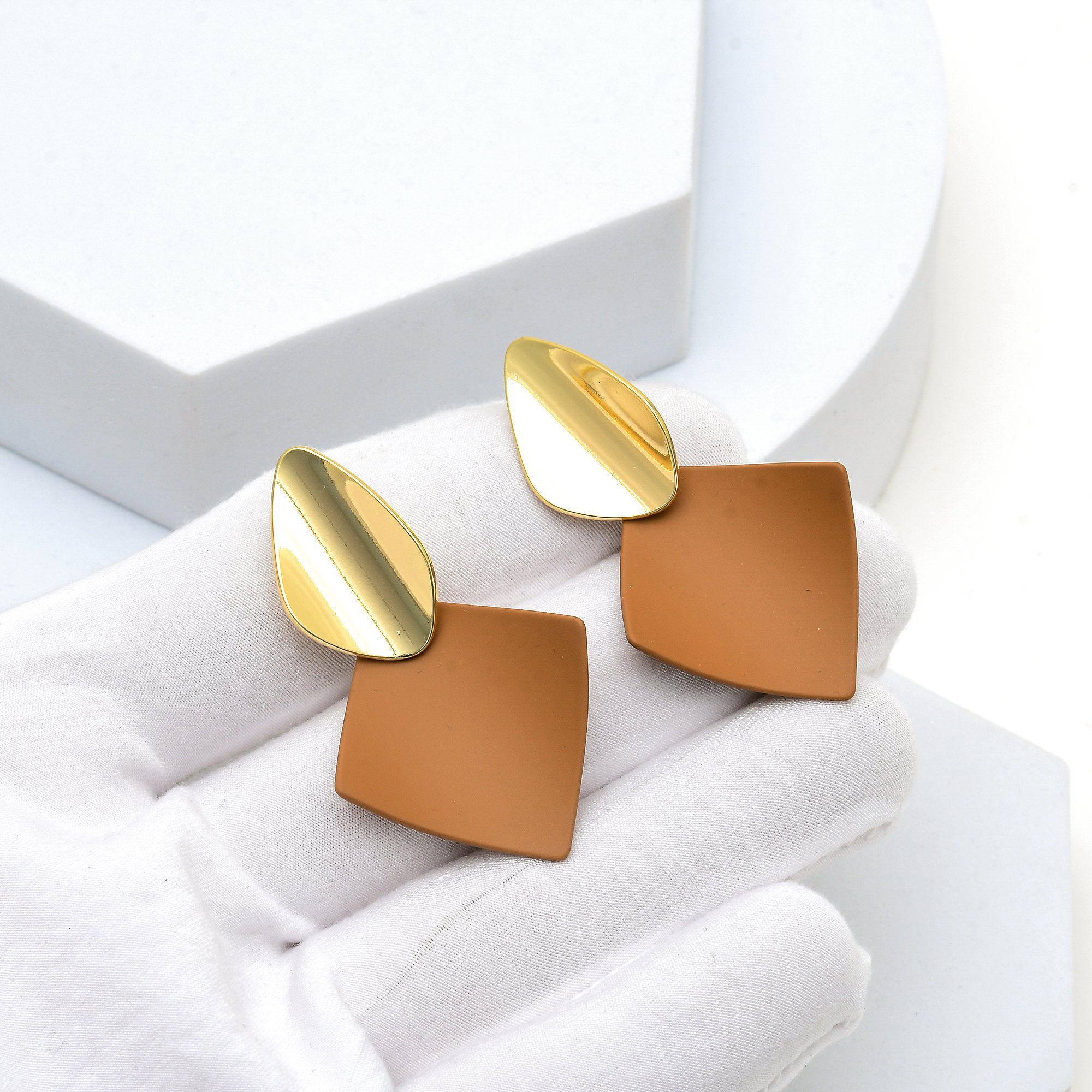 Close up of the mirrored gold finish and matte brown surface of the Terra geometric studs held in hand