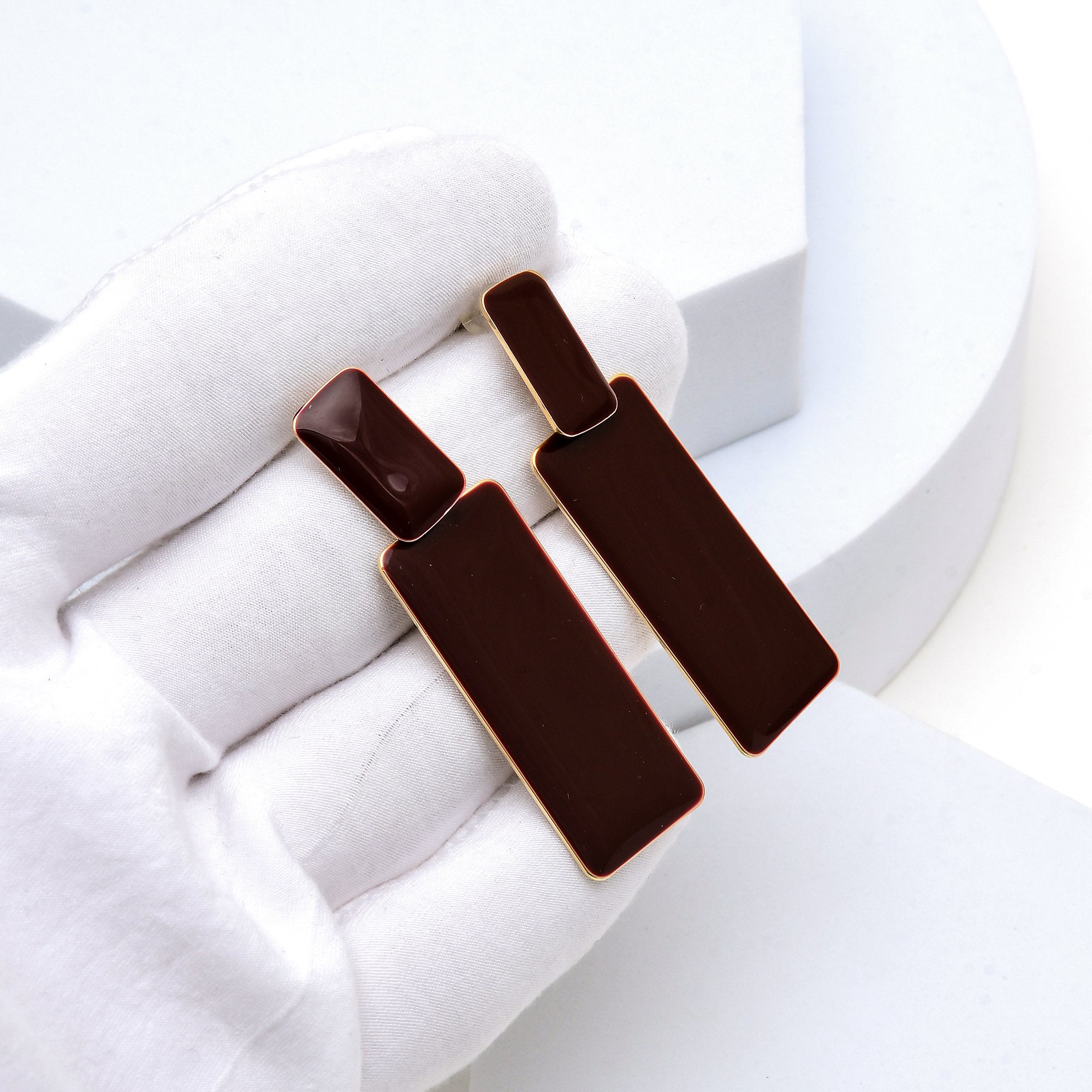 Close up of the polished gold toned backing and glossy brown enamel on the Sienna earrings held in hand