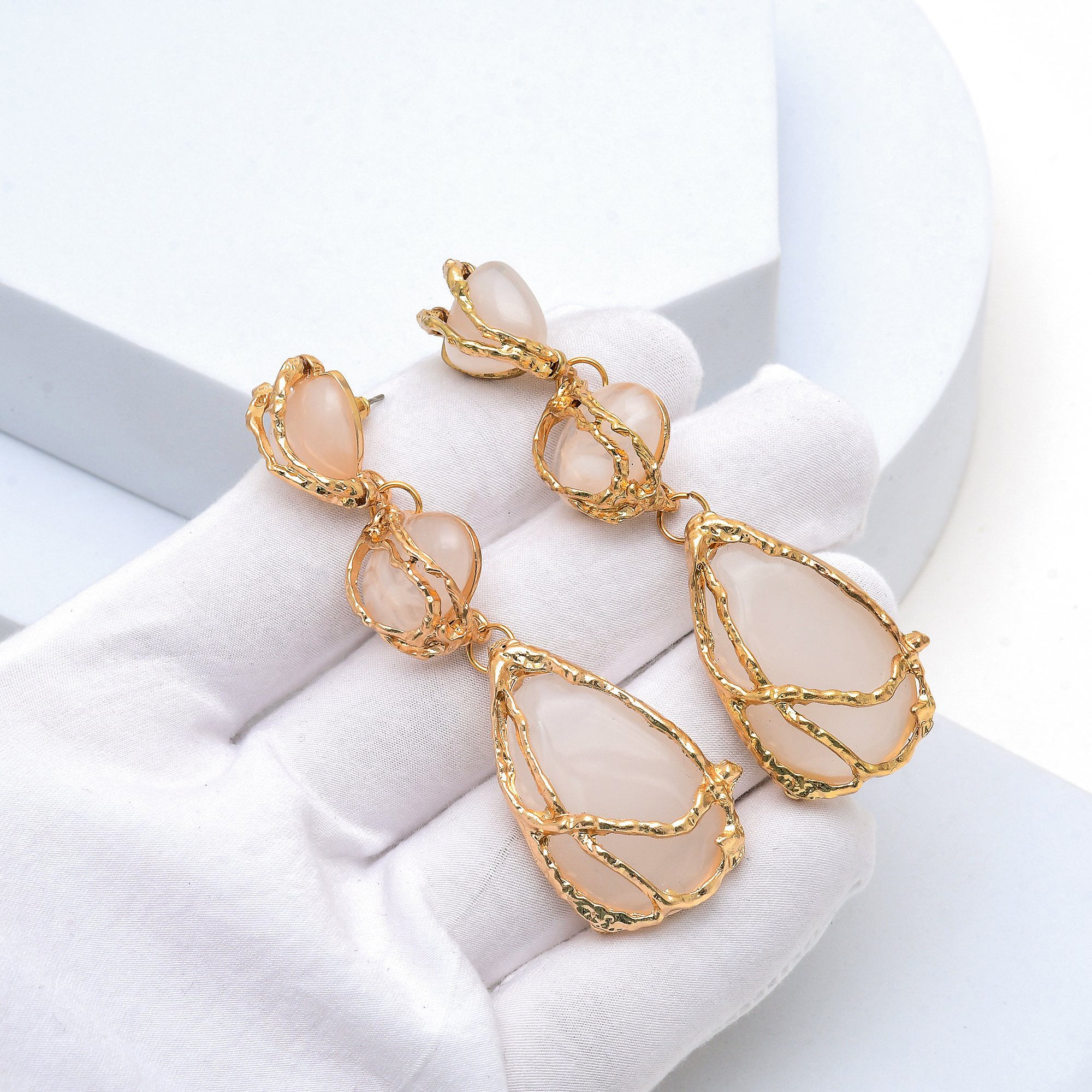 Close up of the textured gold branch detailing and white stones of the Ivory Vine drop earrings held in hand