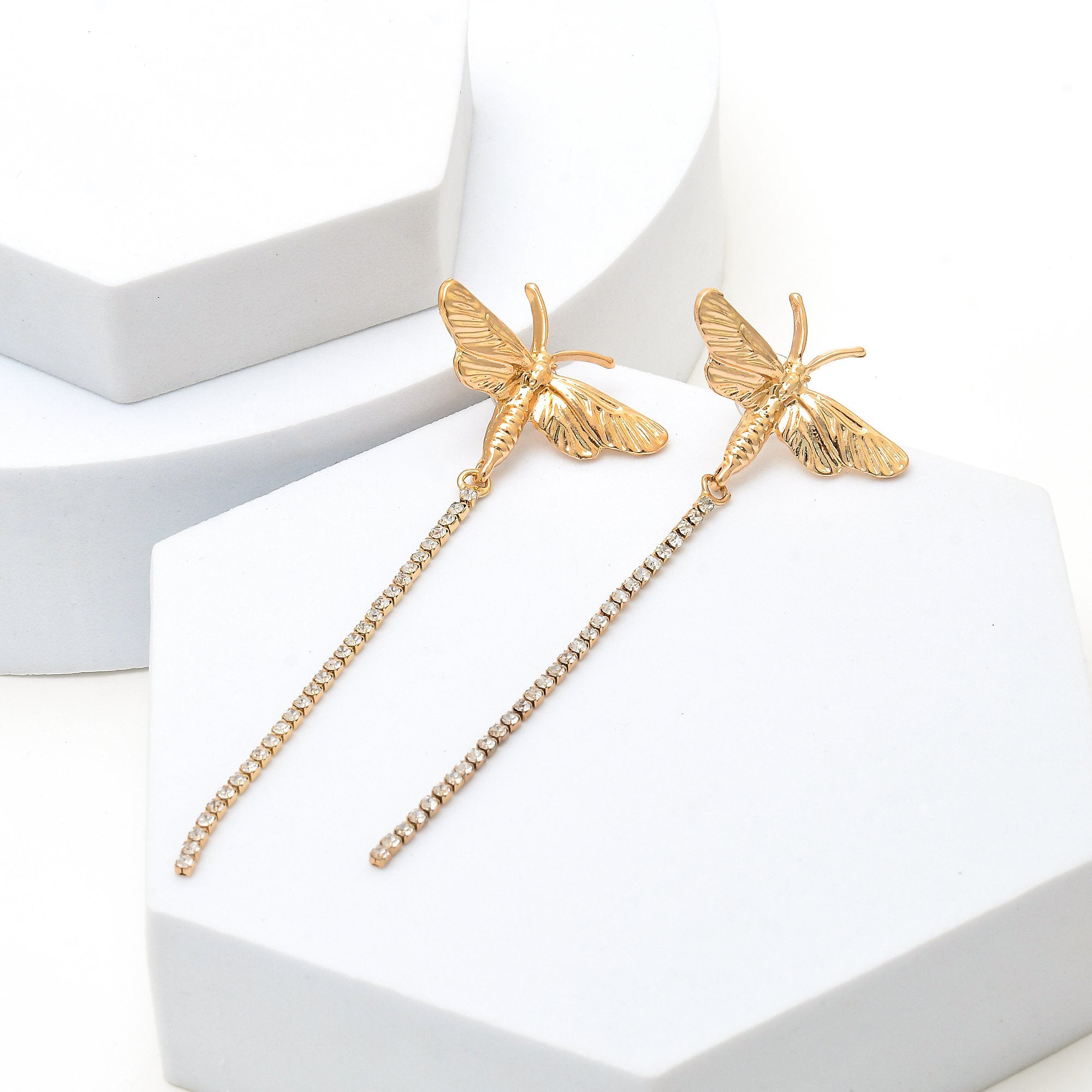 Pair of gold butterfly linear studs arranged on a minimalist background to highlight the crystal detail
