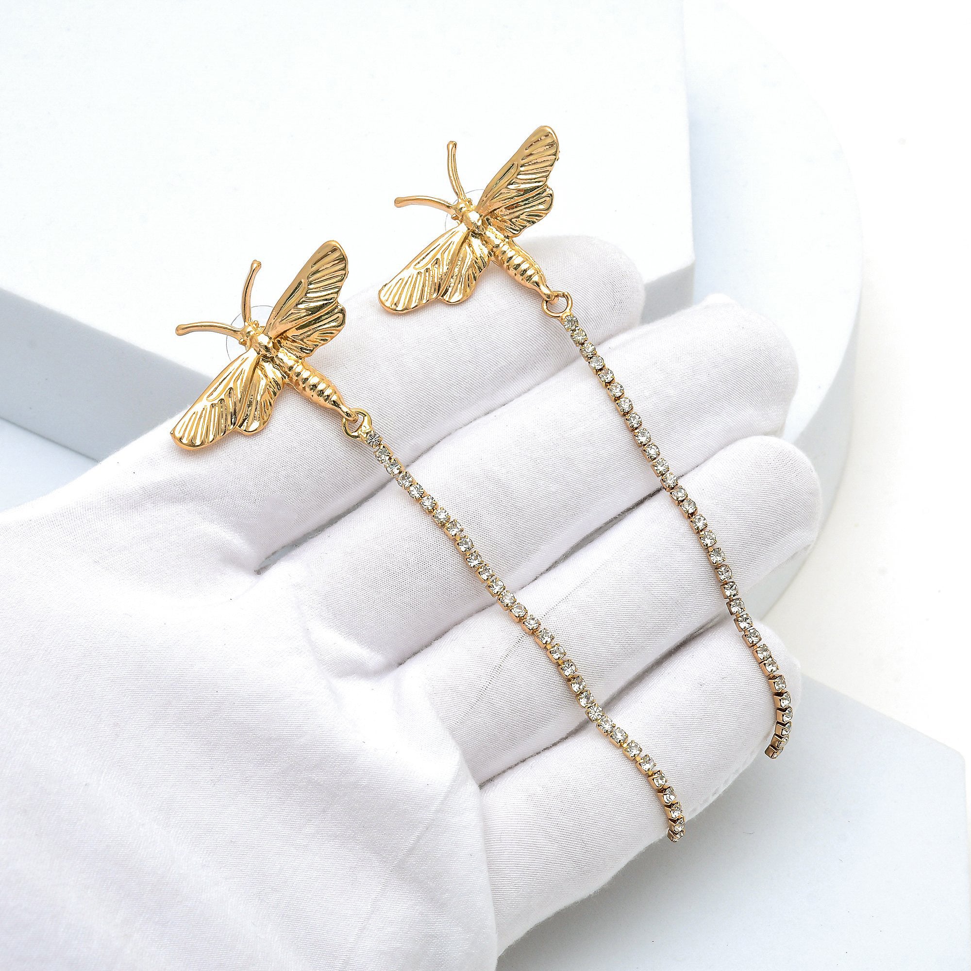Close up of the textured gold butterfly and cubic zirconia chain of the Chrysalis studs held in hand