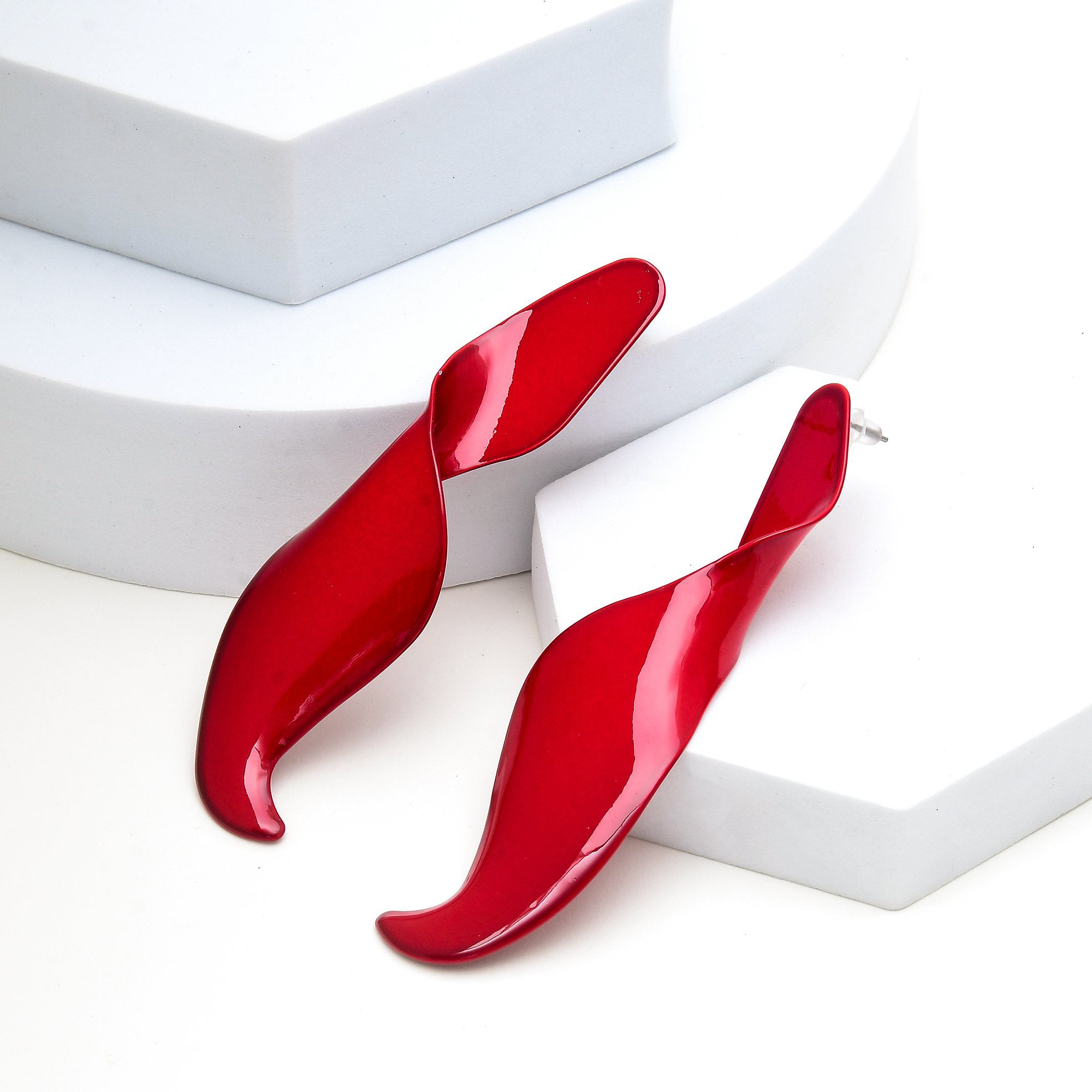 Pair of glossy red architectural ribbon studs on a minimalist display