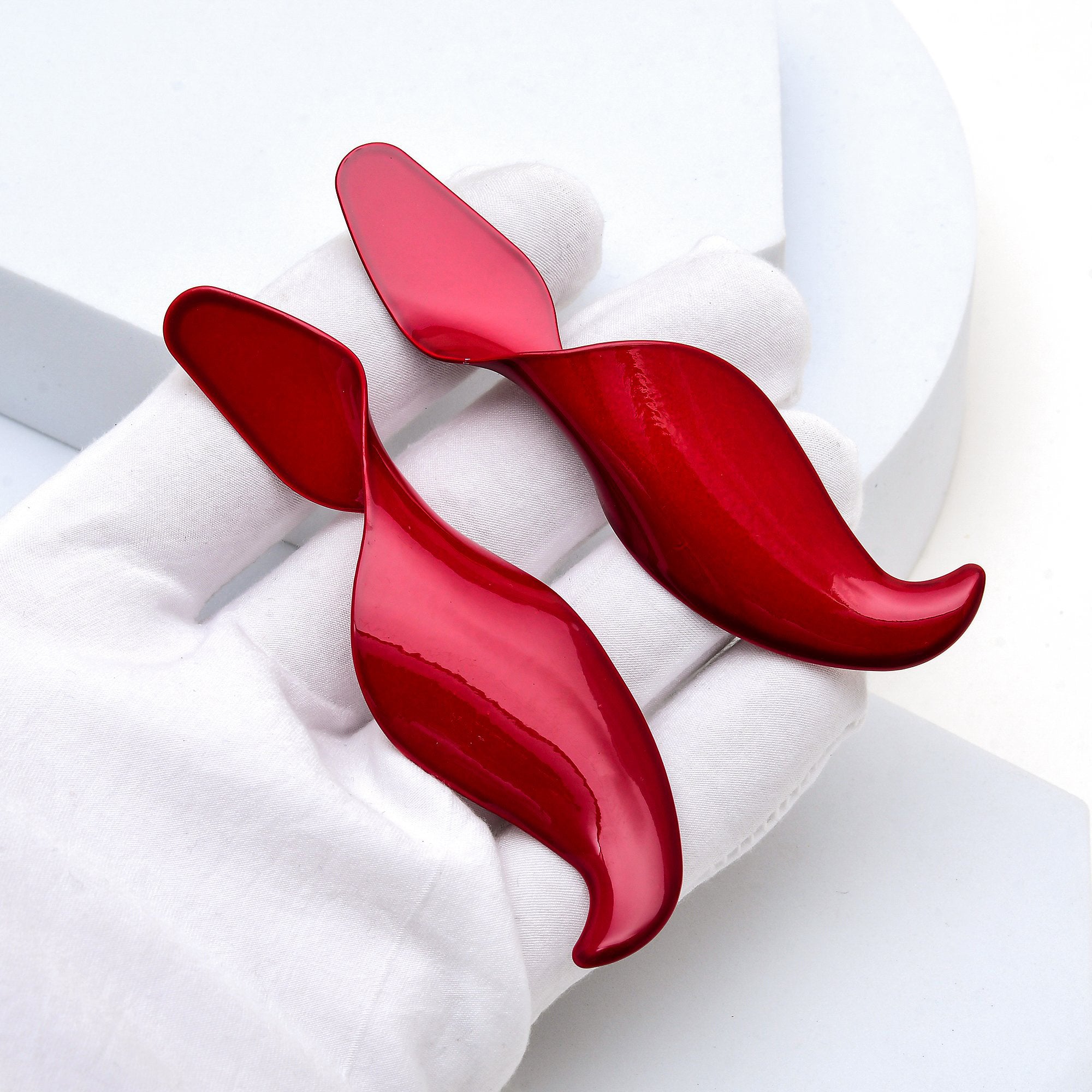 Close up of the high gloss red Crimson Fluidity statement studs in hand