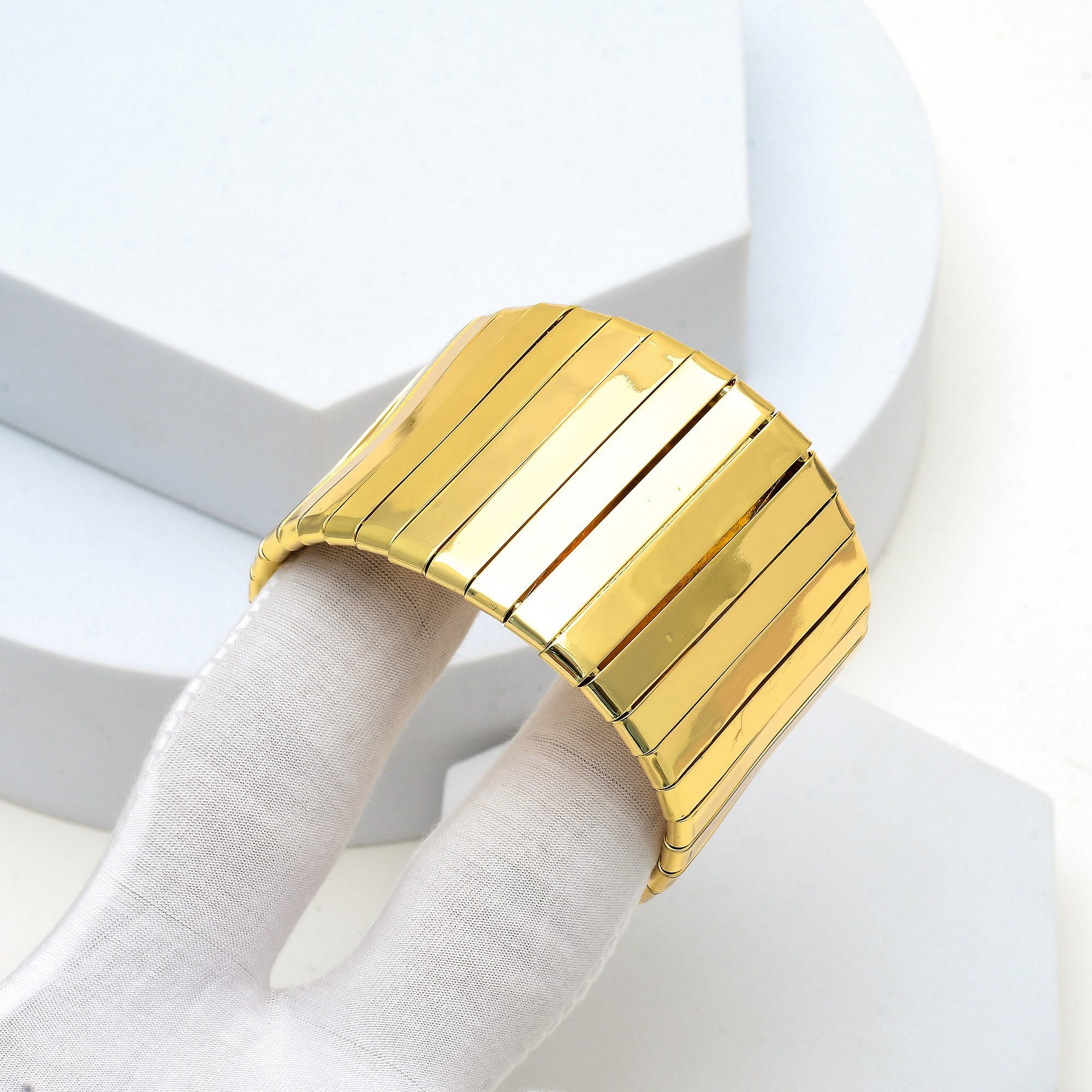 Close up of the mirror finish and flexible articulated panels of the gold toned Aurelia cuff bracelet held in hand