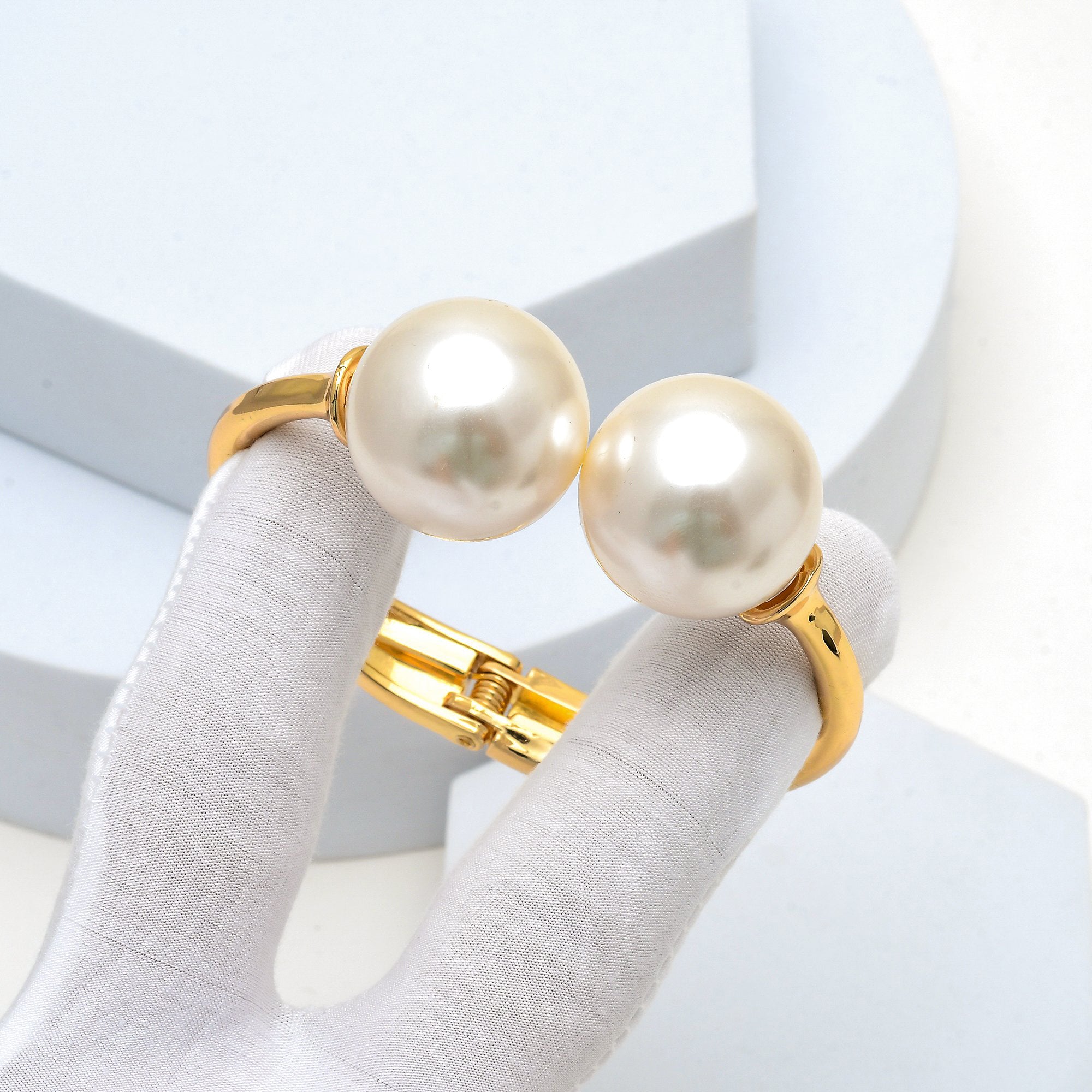 Hand holding the Juno Pearl Bangle to capture the heavy structural quality and liquid-like mirror shine of the gold-toned band