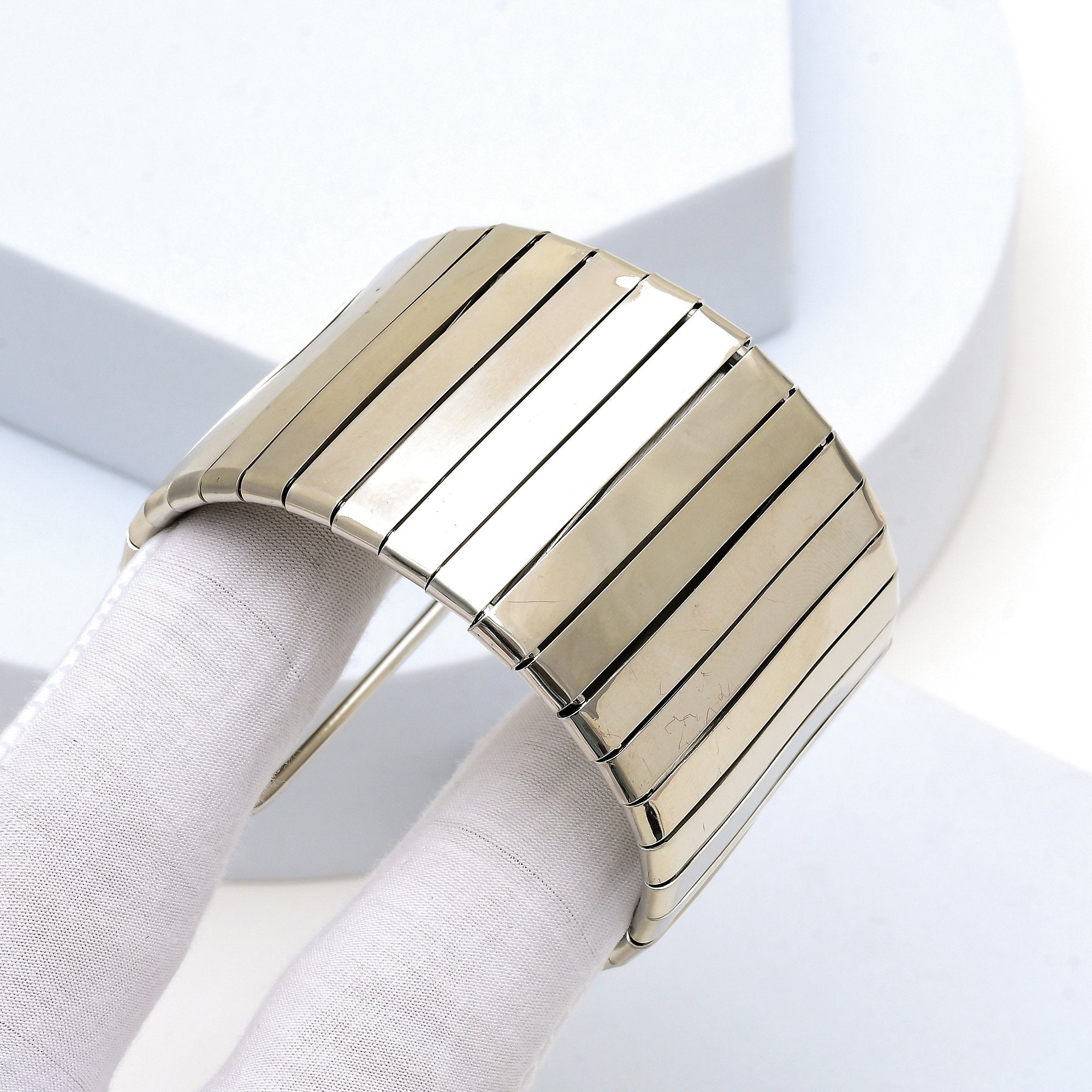 Close up of the mirror finish and flexible articulated panels of the silver toned Aurelia cuff bracelet held in hand