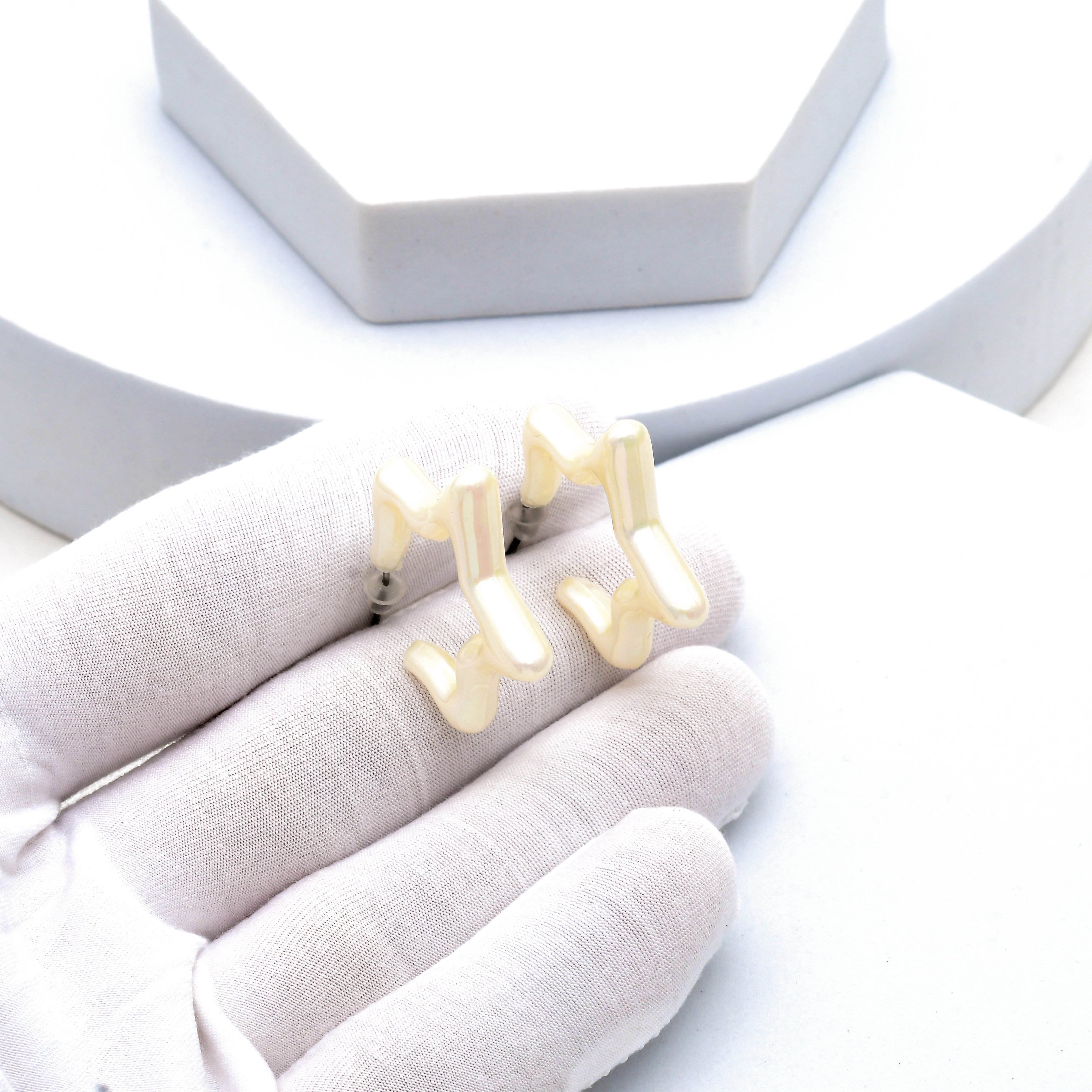 A pair of gold-tone metal earrings shaped like stylized musical notes, held in a white gloved hand against a clean white background with a light gray display stand by Civaro