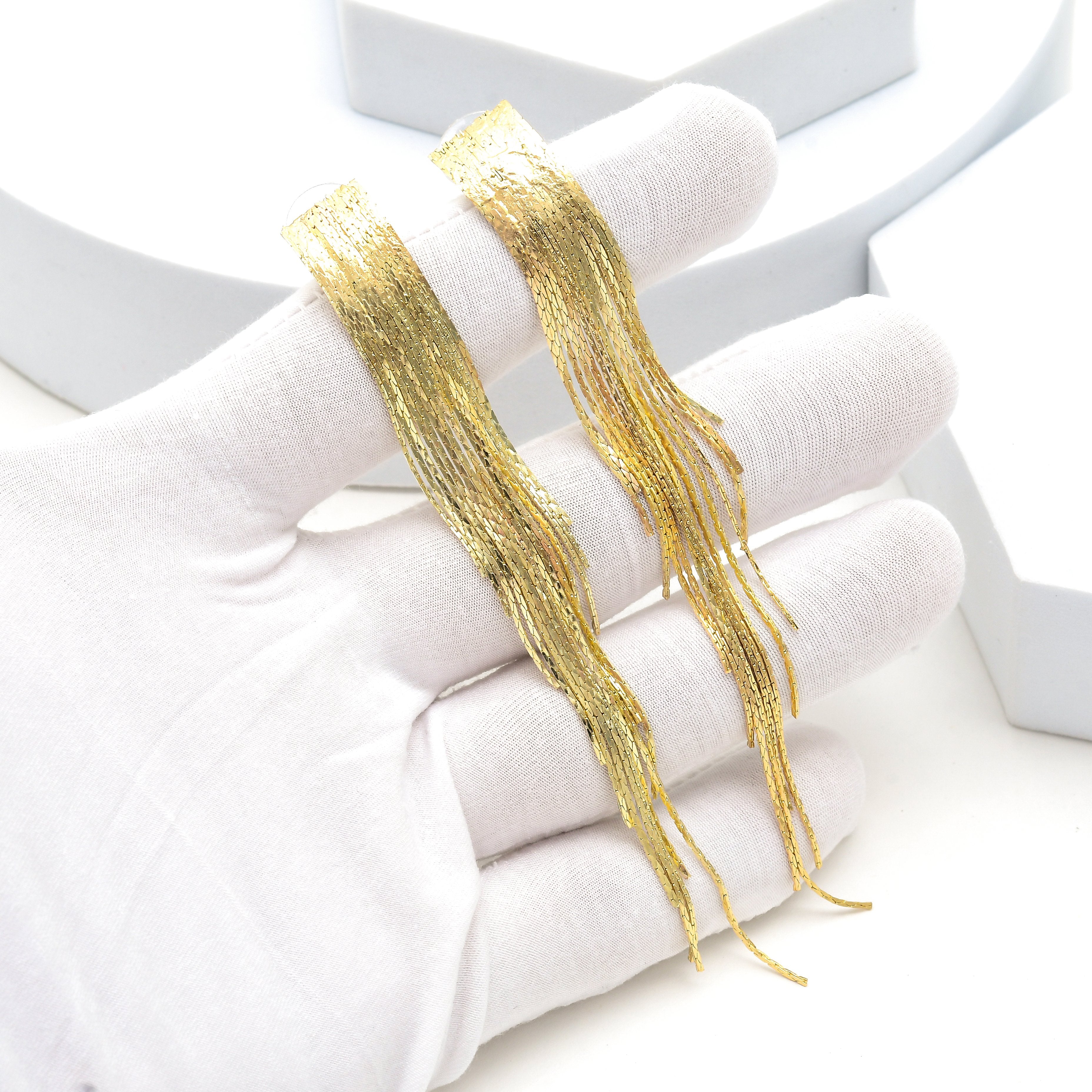 Two long strands of shimmering gold fringe trim held on a white gloved hand against a clean white background by Civaro