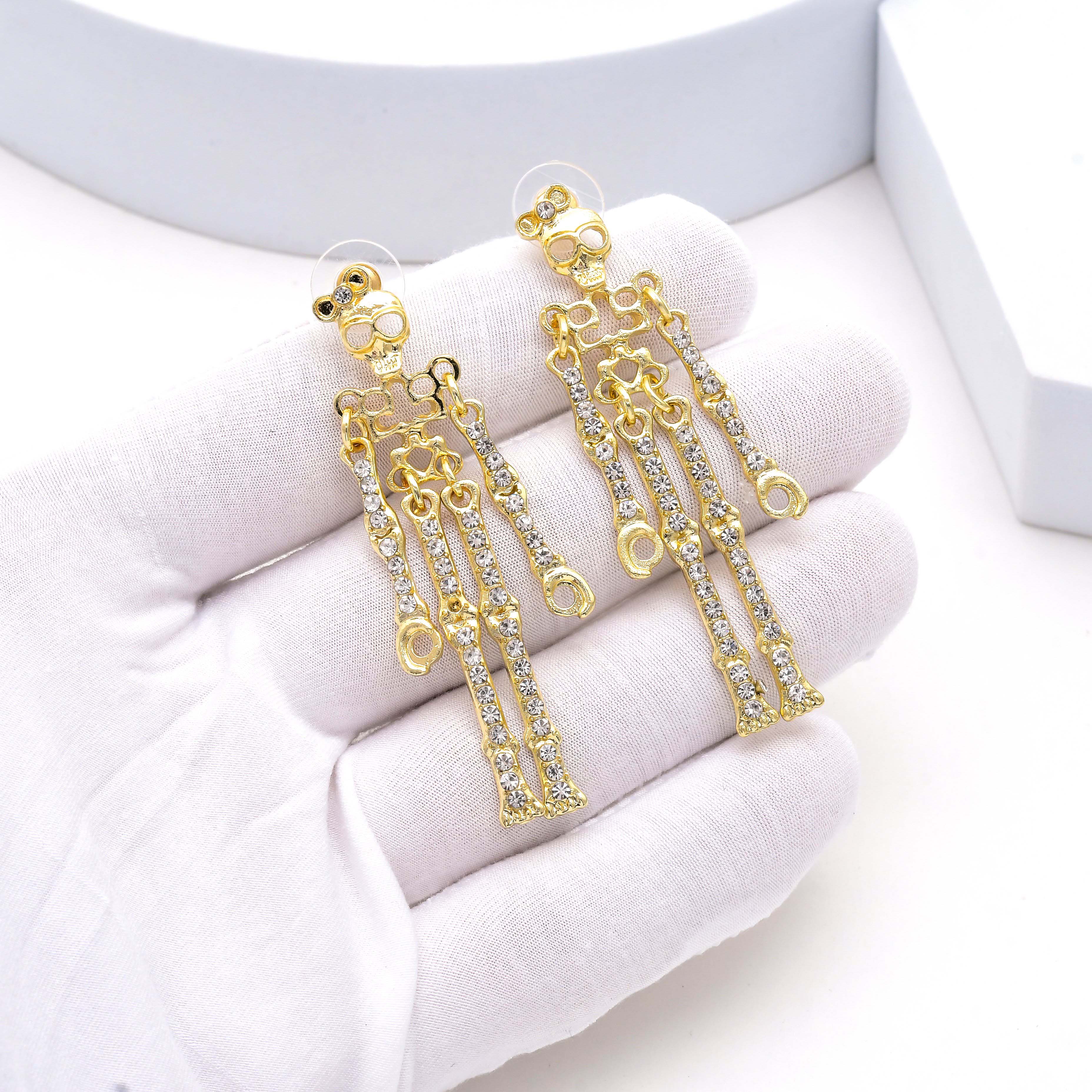 A pair of gold-tone dangle earrings with clear rhinestone-encrusted chains, displayed on a white gloved hand by Civaro