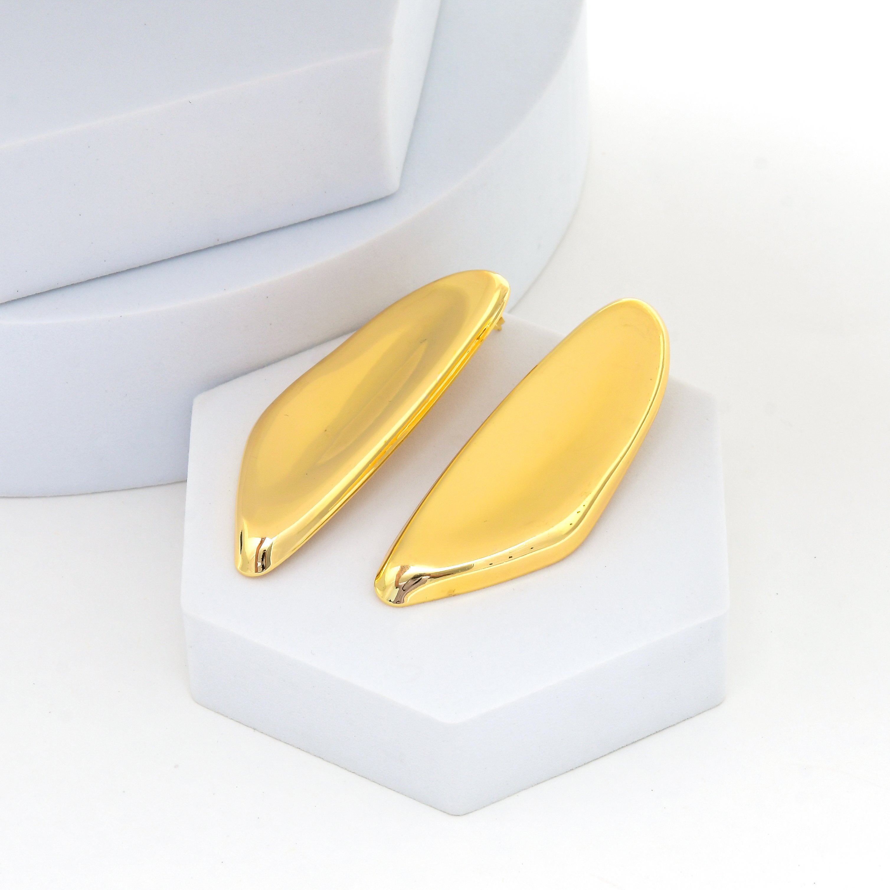 A pair of gold-toned, teardrop-shaped stud earrings displayed on a white geometric stand against a clean white background by Civaro