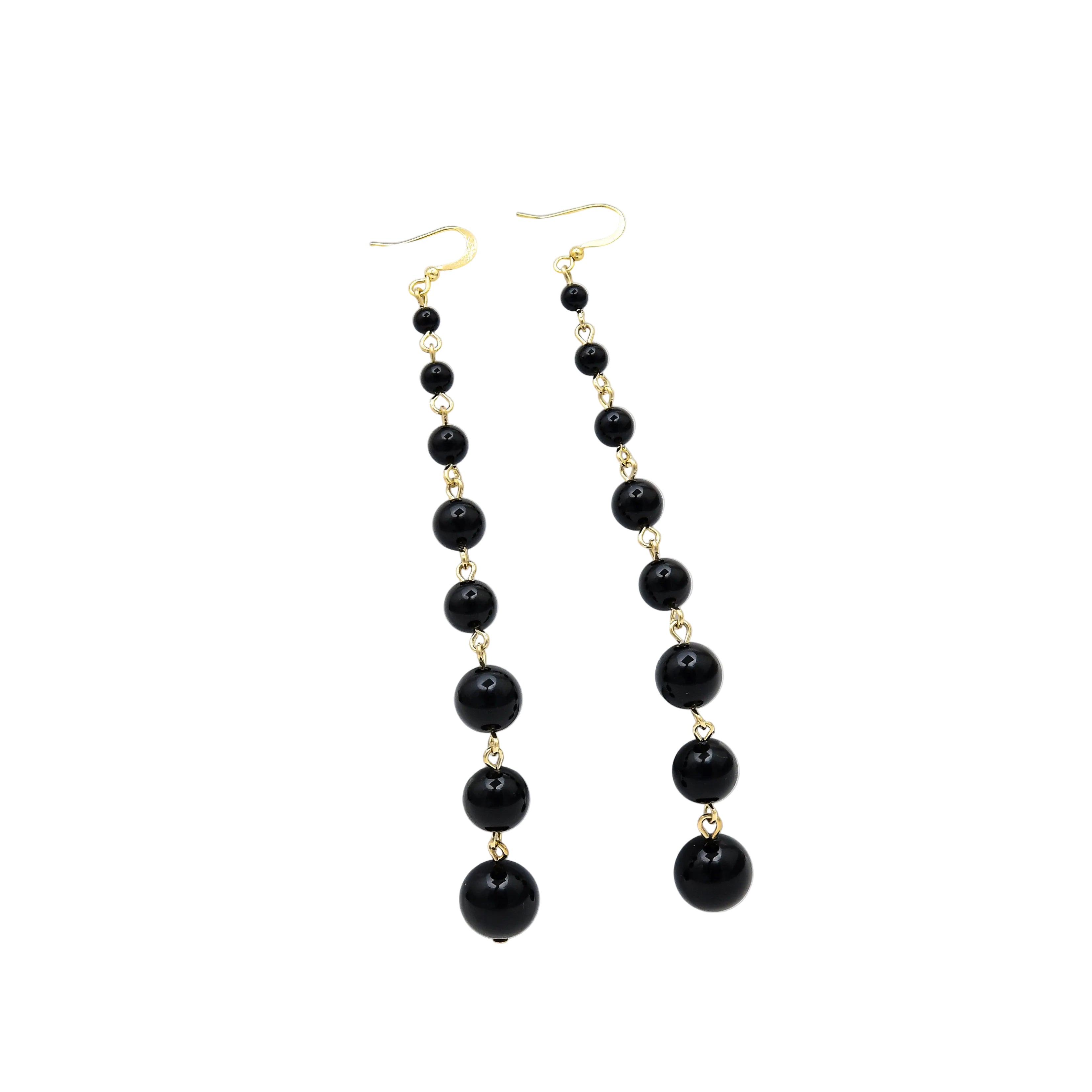 A pair of long drop earrings with small black beads separated by gold links and larger black beads at the bottom, displayed on a white geometric stand against a white background, Black pearl drop earrings crafted with polished gold tone stainless steel featuring graduated pearl beads in a long elegant dangle design by Civaro