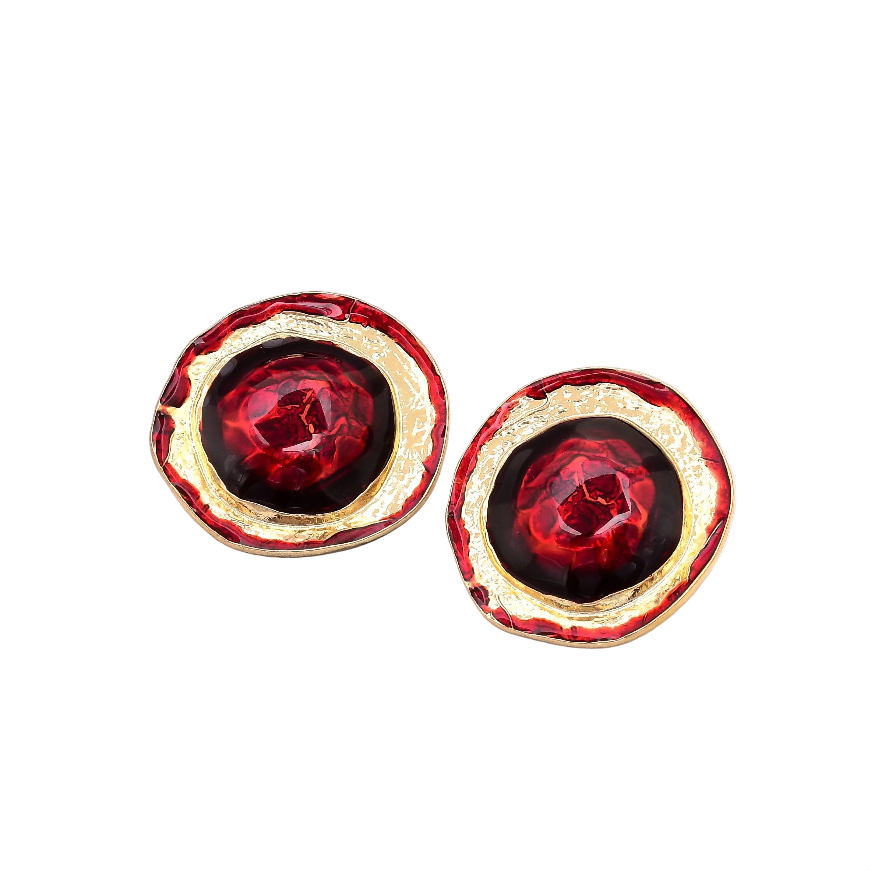 A pair of round gold-tone earrings with textured red enamel and a glossy dark red center, displayed on white geometric blocks,Bold red resin clip-on statement earrings featuring an organic gold tone alloy and brass frame designed for non-pierced ears by Civaro.
