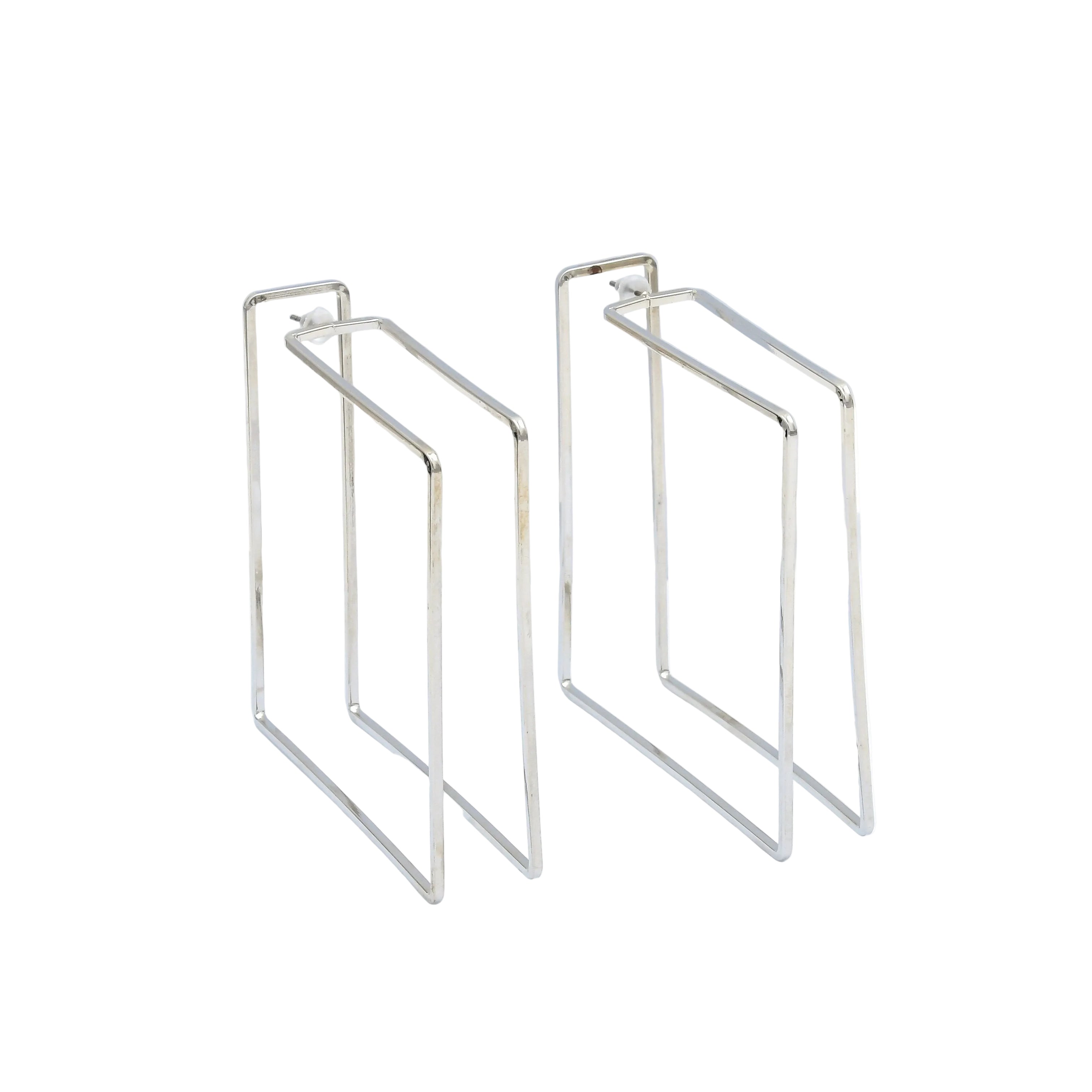 Oversized rectangular stainless steel statement earrings with a polished silver finish designed in a modern geometric silhouette by Civaro.
 A pair of silver-toned geometric wire hoop earrings displayed on a white background