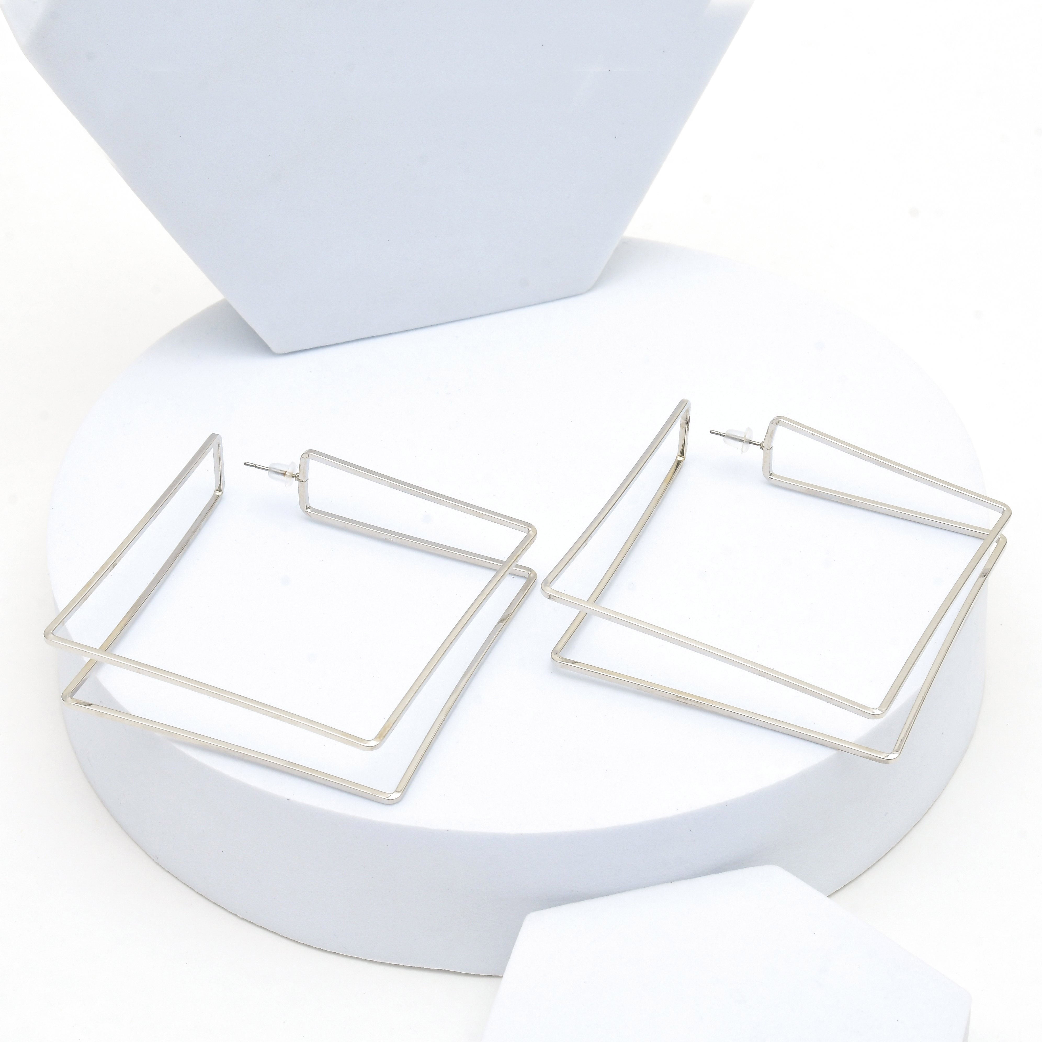Premium stainless steel rectangle drop earrings featuring sleek architectural lines for contemporary fashion by Civaro.
A pair of silver-toned geometric square hoop earrings displayed on a white round pedestal.