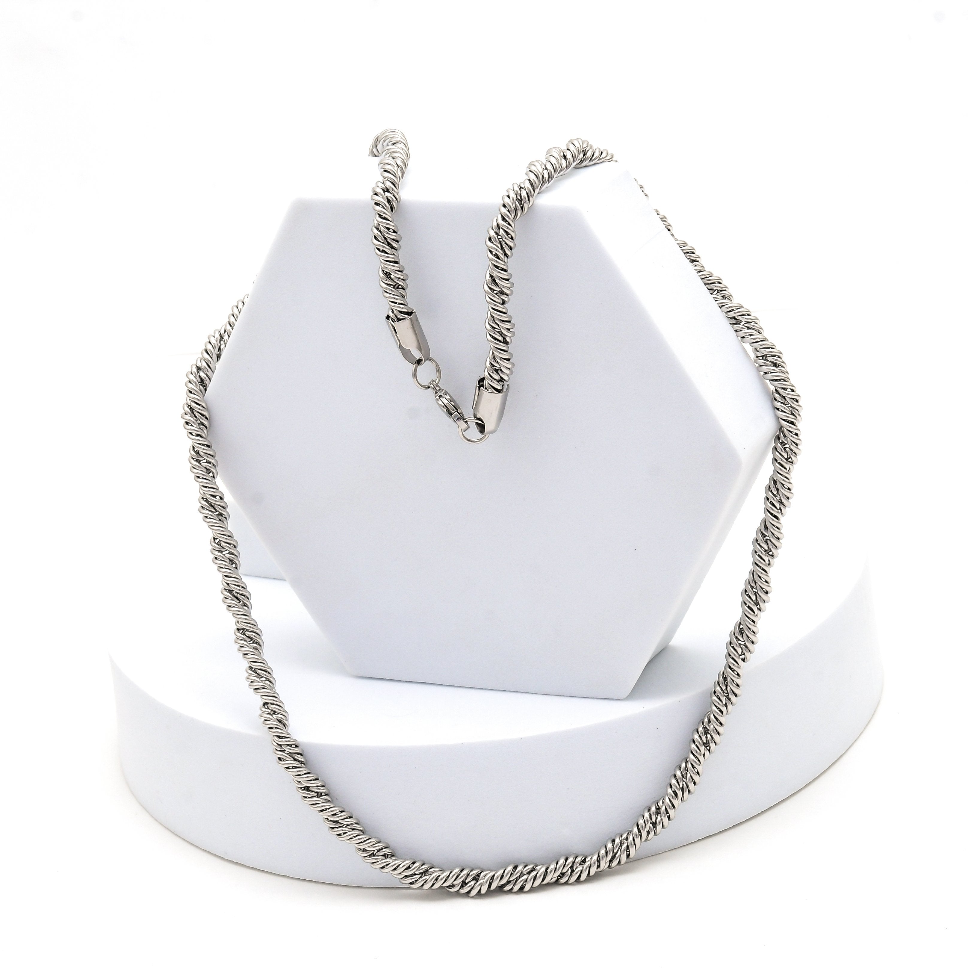 Silver chain for men crafted from premium stainless steel in a classic textured rope chain design by Civaro.
 A silver-toned twisted rope chain necklace draped over a white hexagonal jewelry display stand on a white circular base, photographed against a clean white background.