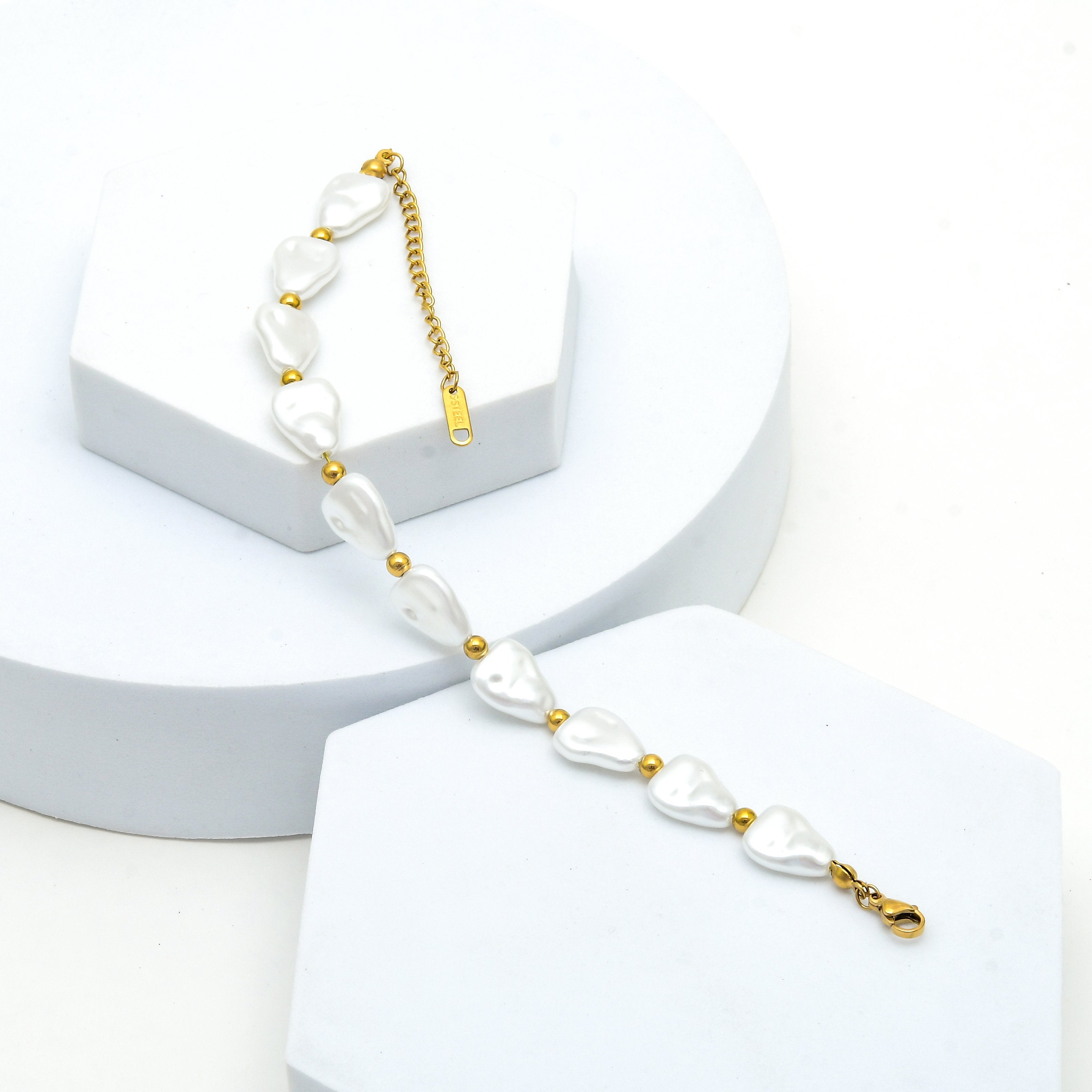 Women's baroque-inspired pearl bracelet featuring irregular white beads separated by delicate gold-tone accents by Civaro.
A gold chain bracelet with irregular white pearl-like beads separated by small gold spacer beads, displayed on white geometric pedestals against a white background.