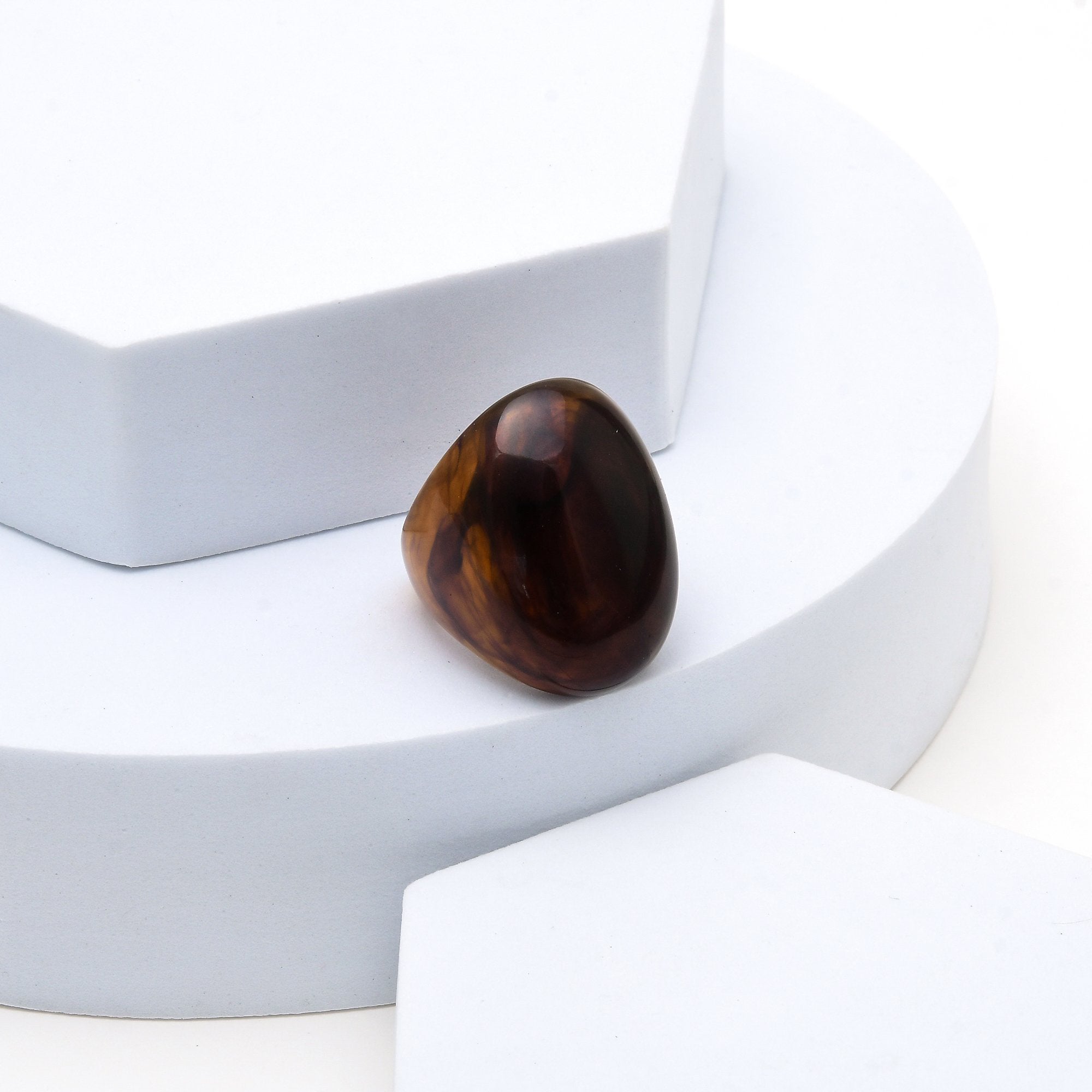 A polished brown tiger's eye stone cabochon resting on a white geometric display stand.
