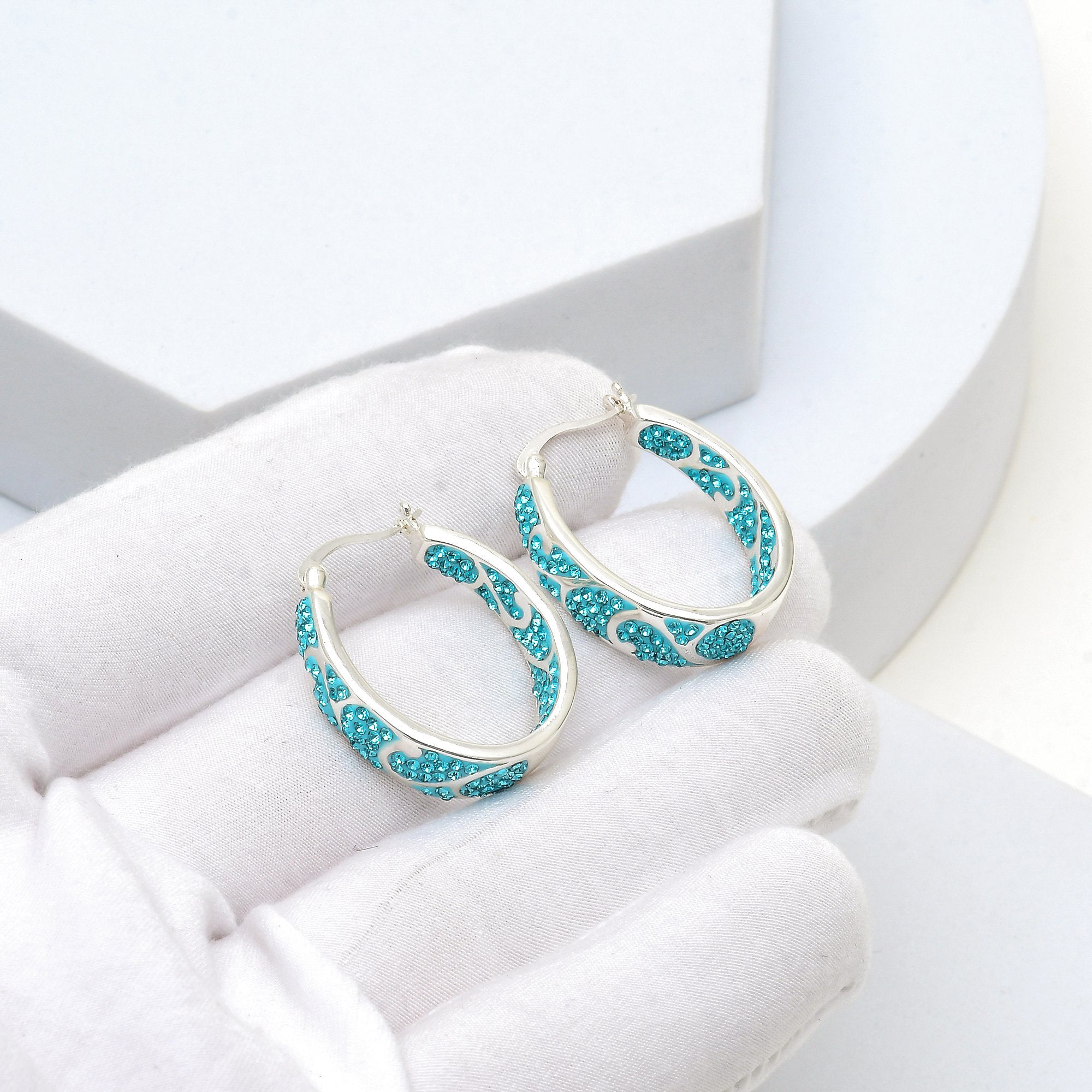 Close-up of the handcrafted open-work design and precision hand-set teal crystals on the Signature Teal Swirl hoops