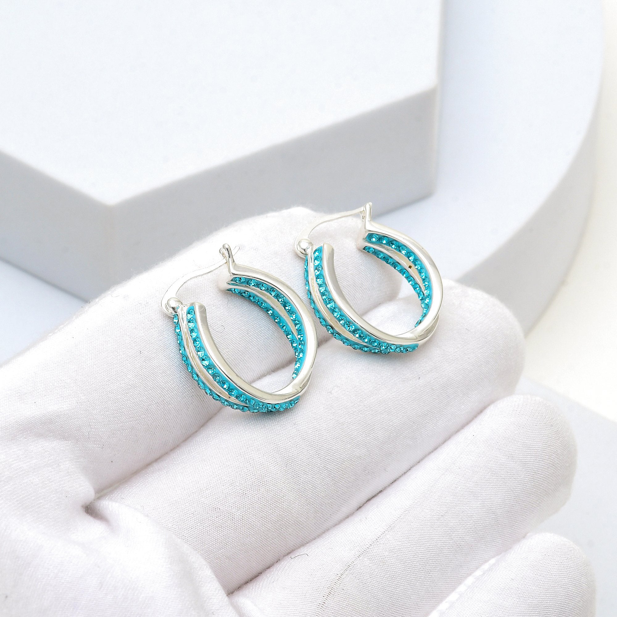 Close up of the precise double-row pavé crystal setting and silver plating on the Cyan Glace hoop earrings held in hand