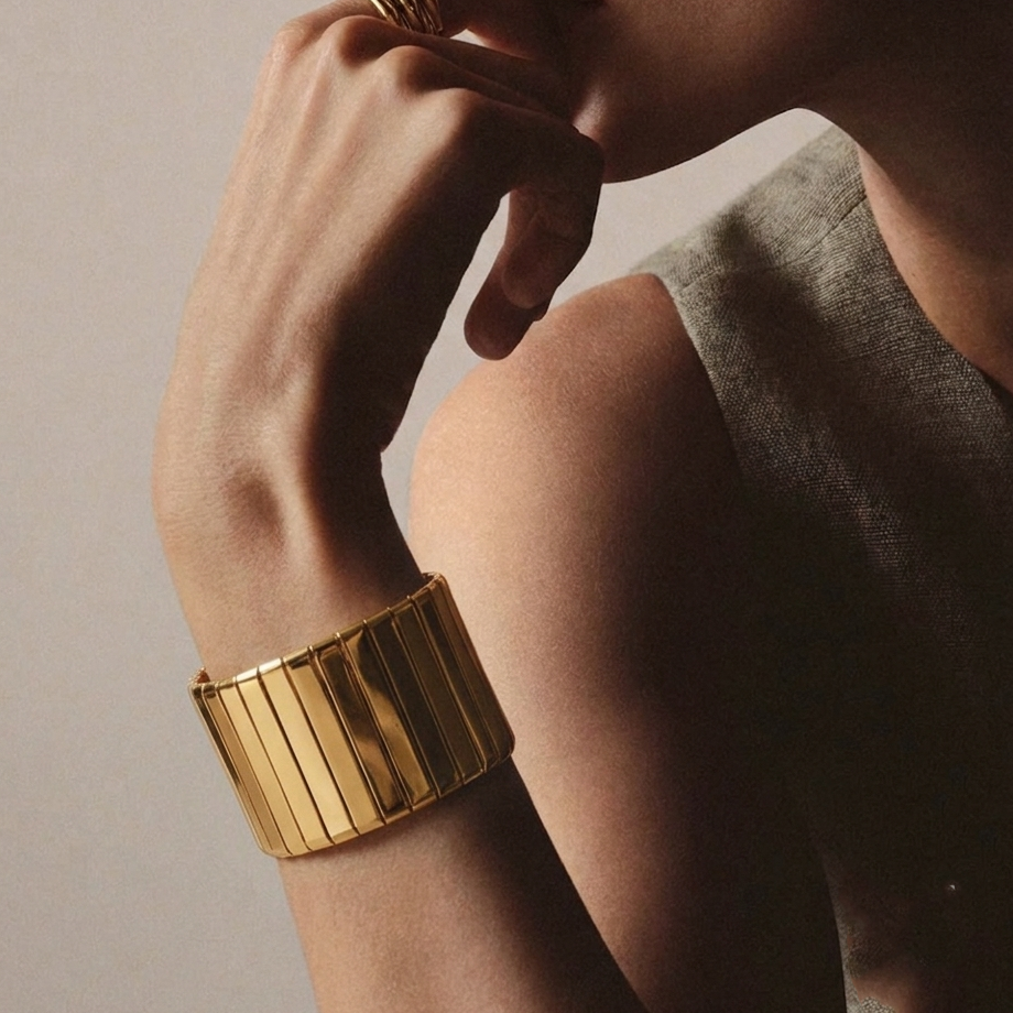 Model styling the wide gold toned Aurelia segmented cuff bracelet on the wrist over a sharp blazer cuff