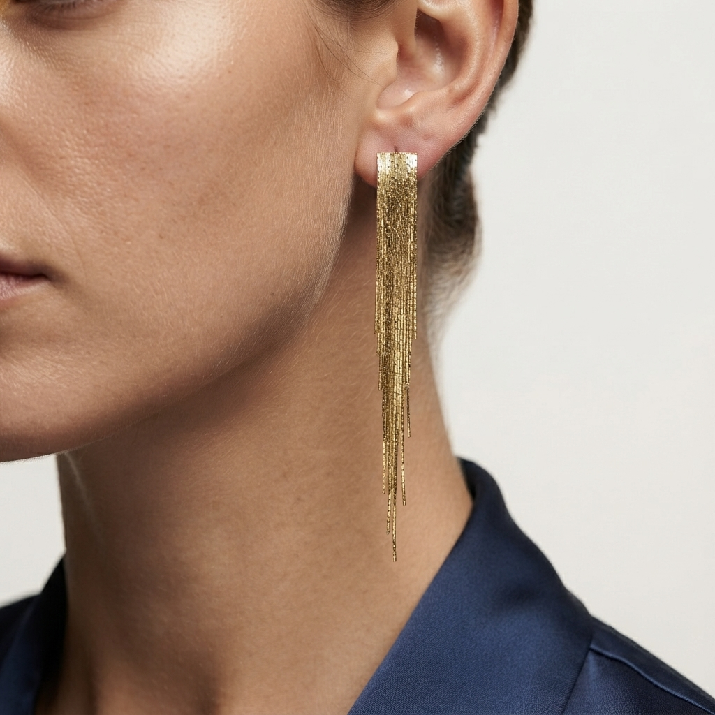 A close-up of a model's ear wearing a long, dangling gold earring with multiple thin fringe strands by Civaro
