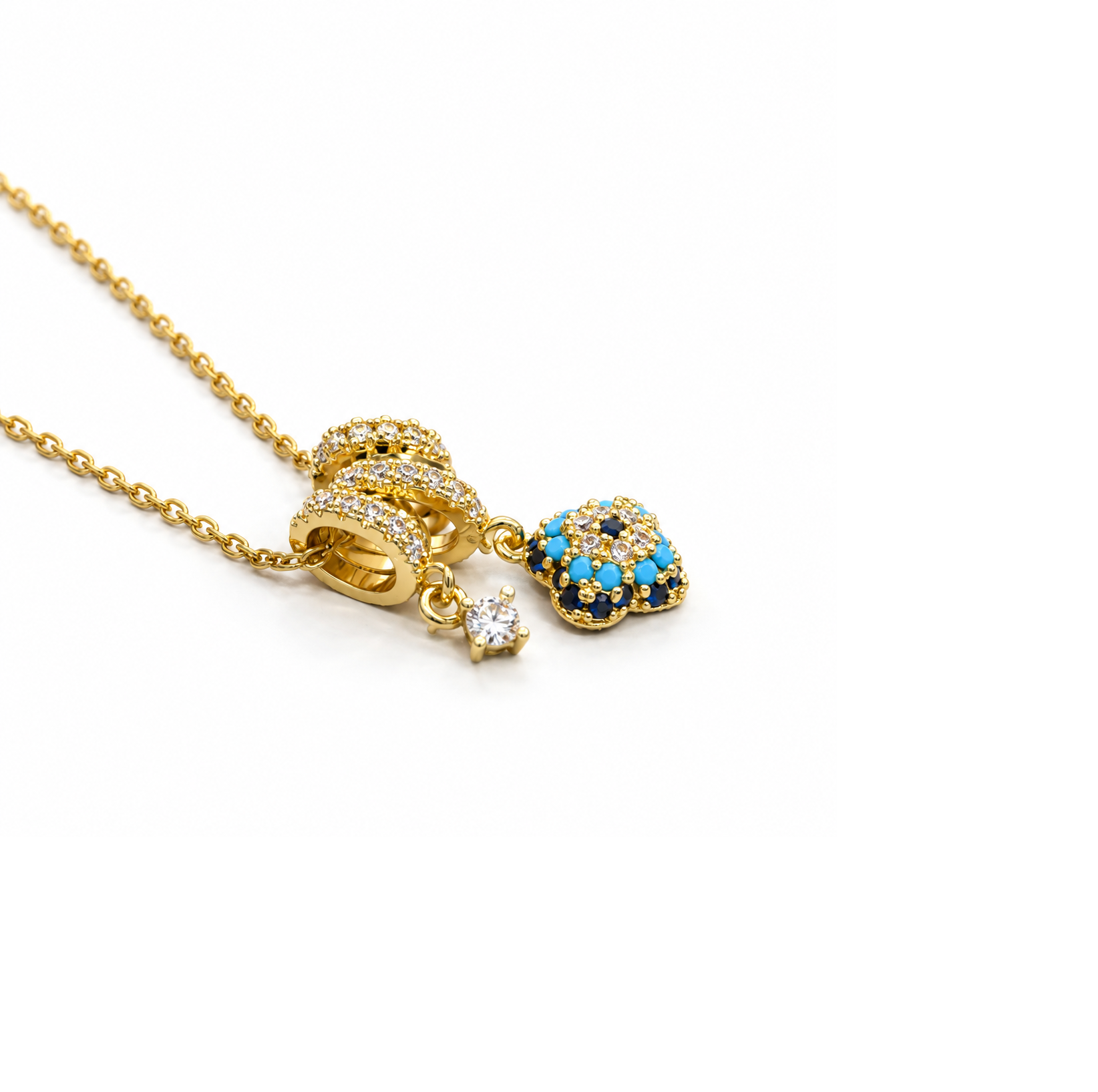 Gold-tone charm necklace with blue evil eye inspired centerpiece and clear stones by Civaro
A gold chain necklace featuring a detailed pendant with a gold heart-shaped charm accented by blue and white stones, alongside a small dangling clear gemstone charm, set against a plain white background.