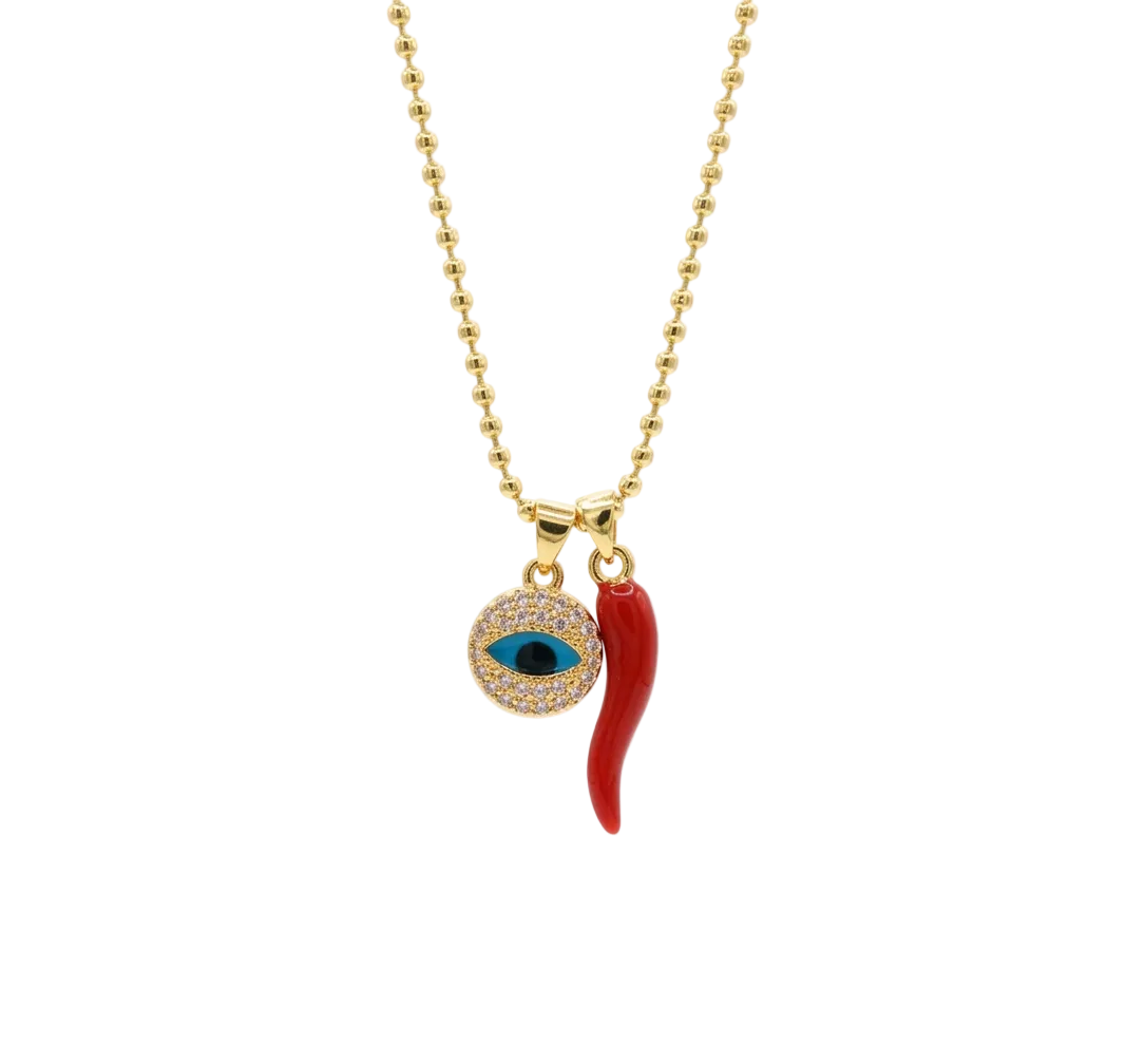 Gold ball chain necklace with a double pendant: a red chili pepper charm and a circular evil eye charm paved with small clear stones with a blue and black center, on a white background.