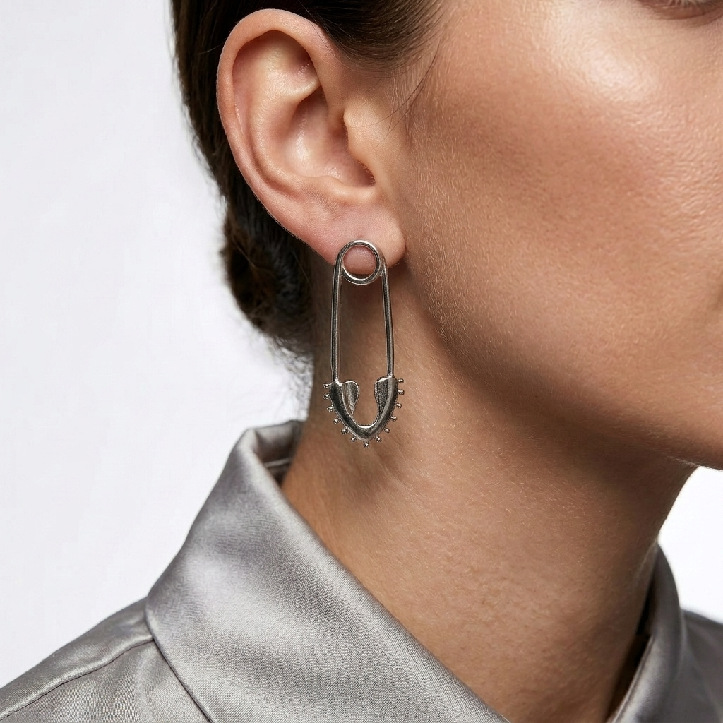     Modern minimalist silver safety pin earrings displayed on a white jewelry stand.