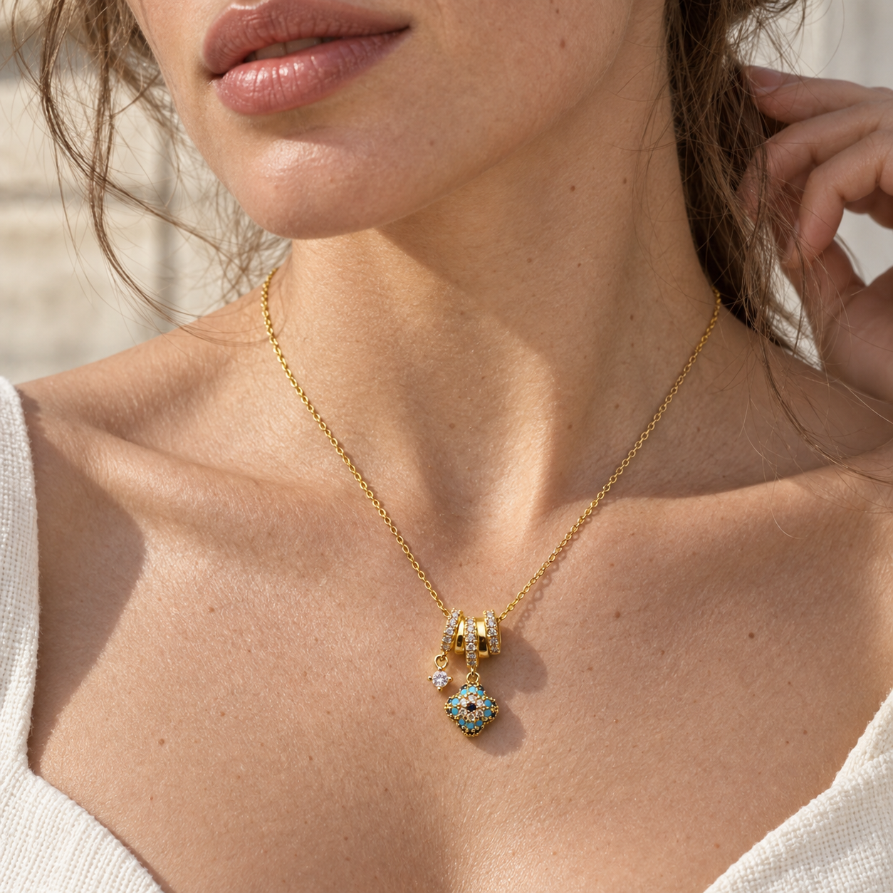Nazar charm necklace with turquoise-blue stones and sparkling gold-tone pendant by Civaro
A close-up lifestyle shot of a model wearing a delicate gold chain necklace with a multi-pendant charm set with turquoise and white stones.