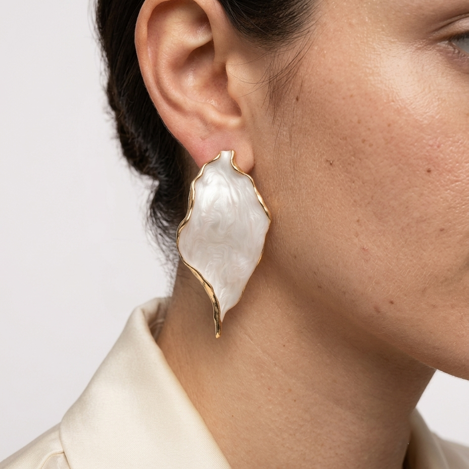     Sculptural white acrylic earrings with flowing organic silhouette and gold-tone detailing.