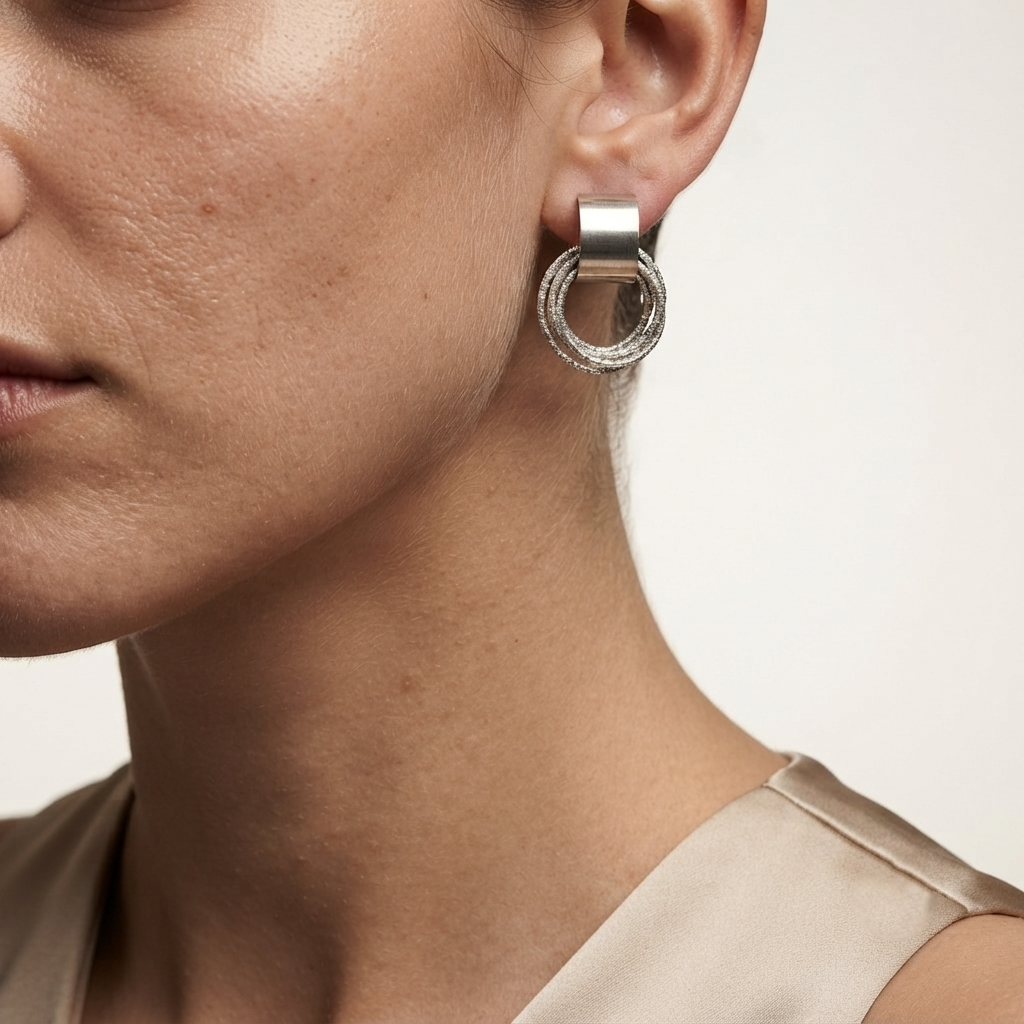 A close-up of a woman's ear wearing a silver hoop earring with a textured, beaded outer ring and a solid inner ring by Civaro