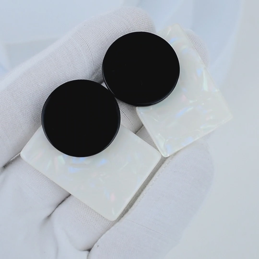Video showcasing black and opal geometric statement earrings with iridescent detailing, Video showing the shifting pearlescent reflections on the white acrylic resin surface of the Onyx Aura earrings