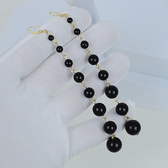 Long beaded pearl earrings featuring polished black pearls and gold tone stainless steel hardware for elegant everyday styling by civaro