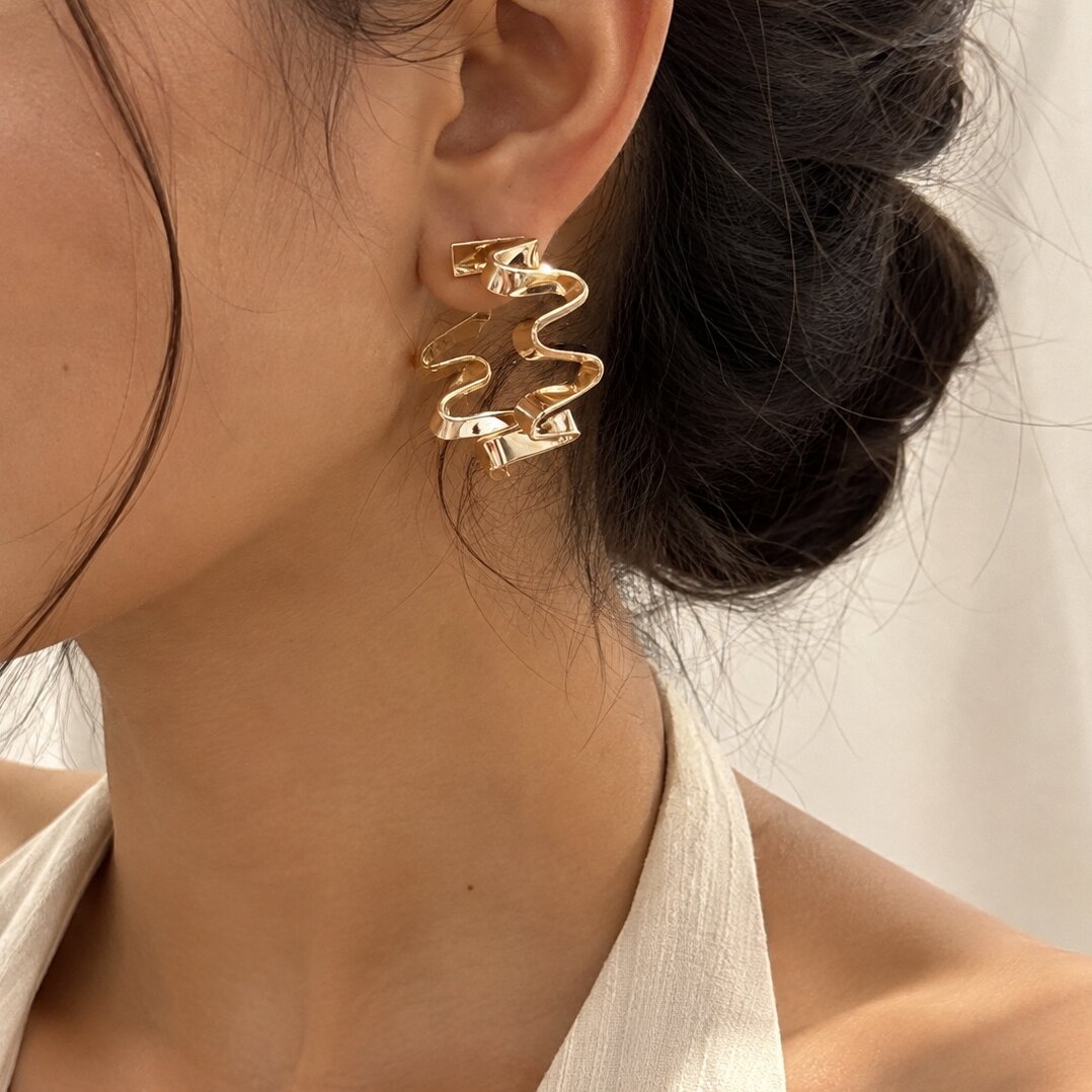 Gold zigzag hoop earrings with sculptural wavy design in stainless steel by Civaro
A close-up of a model's ear wearing a gold-toned, multi-strand twisted wire earring.